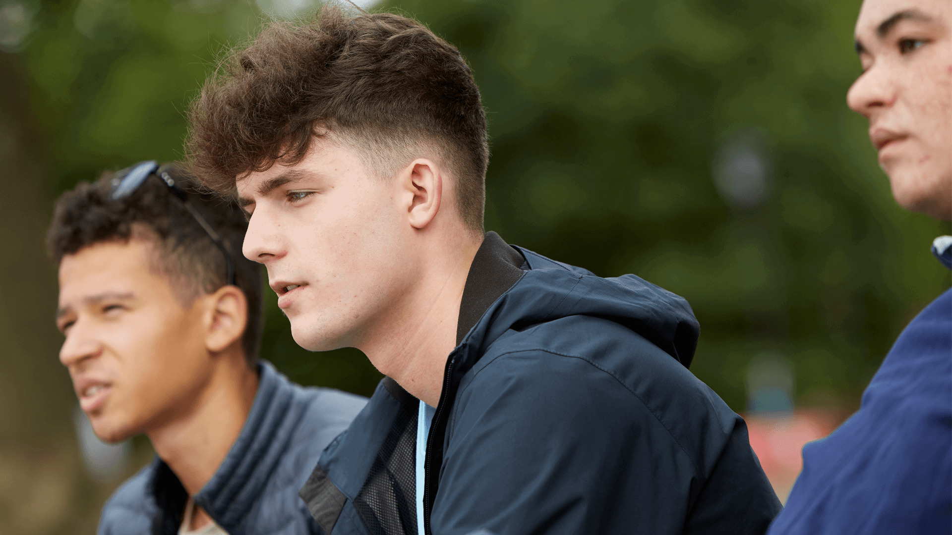 Three boys sitting together on a park bench. They are all looking ahead with serious expressions.