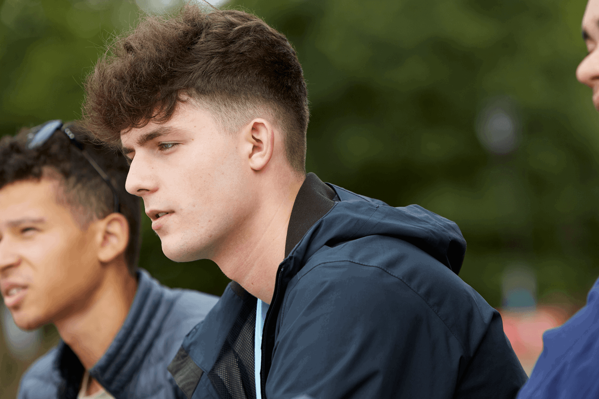 Three boys sitting together on a park bench. They are all looking ahead with serious expressions.