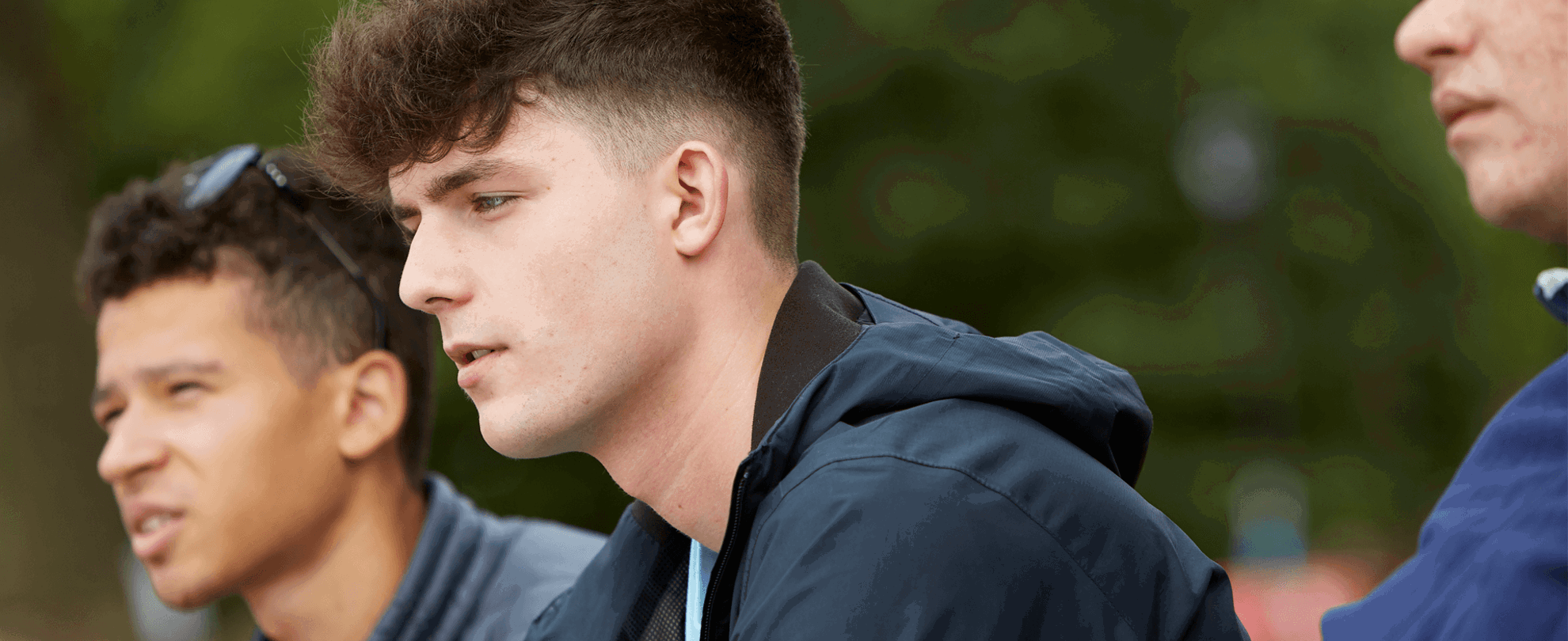 Three boys sitting together on a park bench. They are all looking ahead with serious expressions.