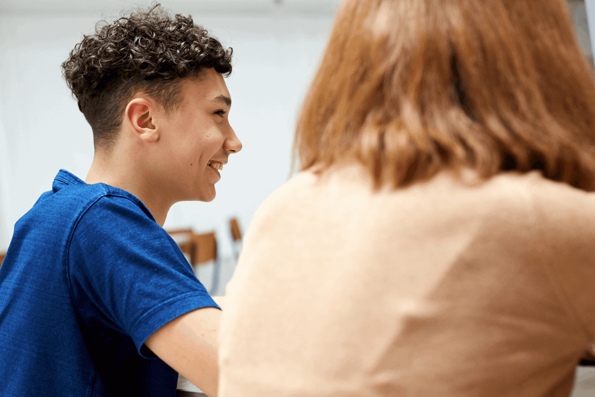 backshot-of-a-boy-with-short-curly-hair-and-wearing-blue-shirt-laughing-beside-a-girl-wearing-beige-shirt-with-face-unseen-while-inside-a-classroom