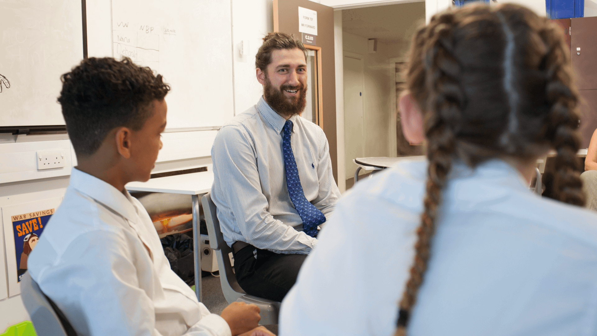 teacher smiling as he sits with two of his students in class