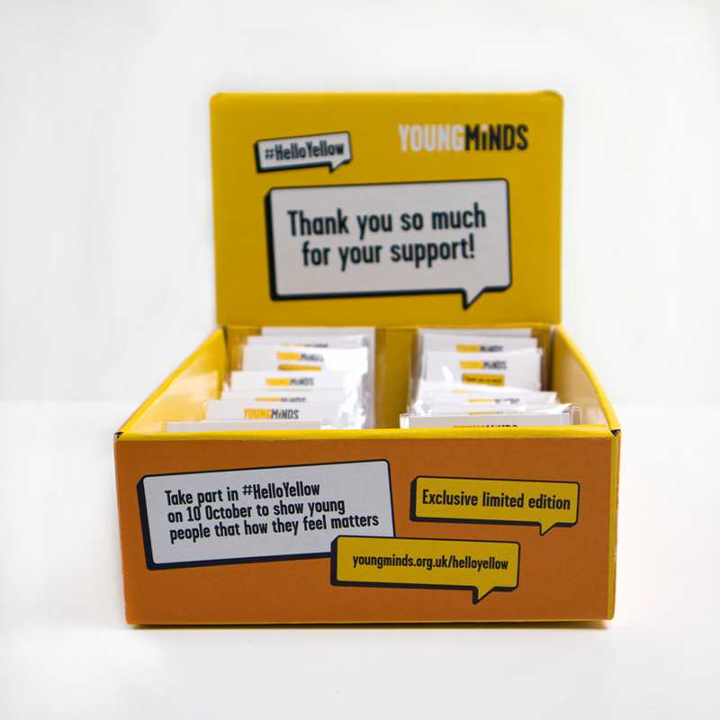 A yellow and orange box containing 30 #HelloYellow pin badges. The front panel of the box says 'Take part in #HelloYellow on 10 October to show young people that how they feel matters.' The back panel says 'Thank you so much for your support!'