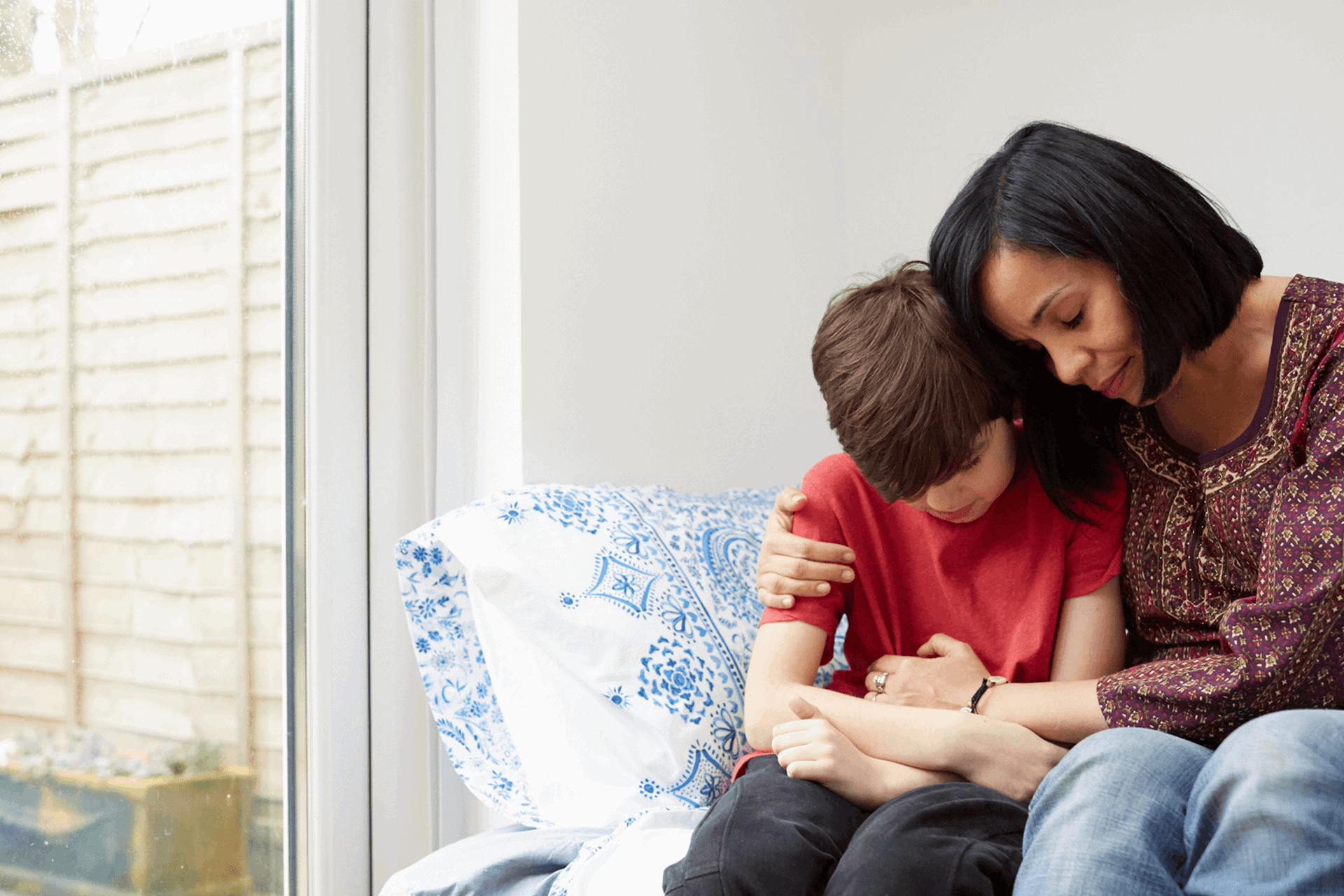 A mother comforting her young son at home in a conservatory