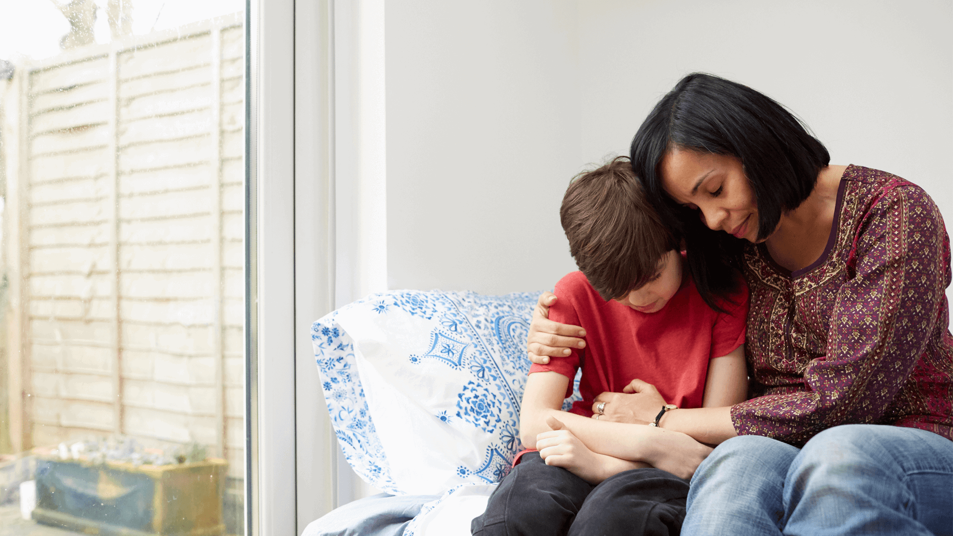 A mother comforting her young son at home in a conservatory