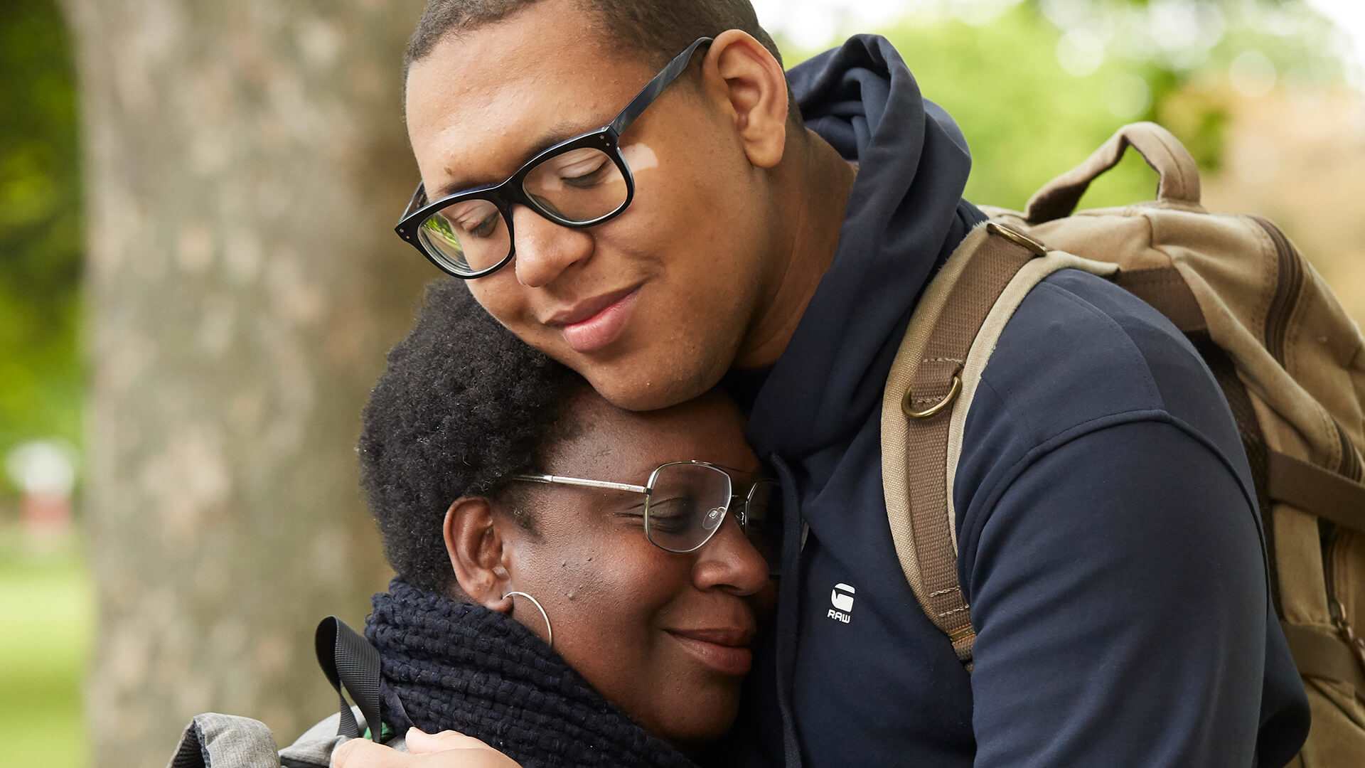 A mother and son smiling hugging in a park by a tree