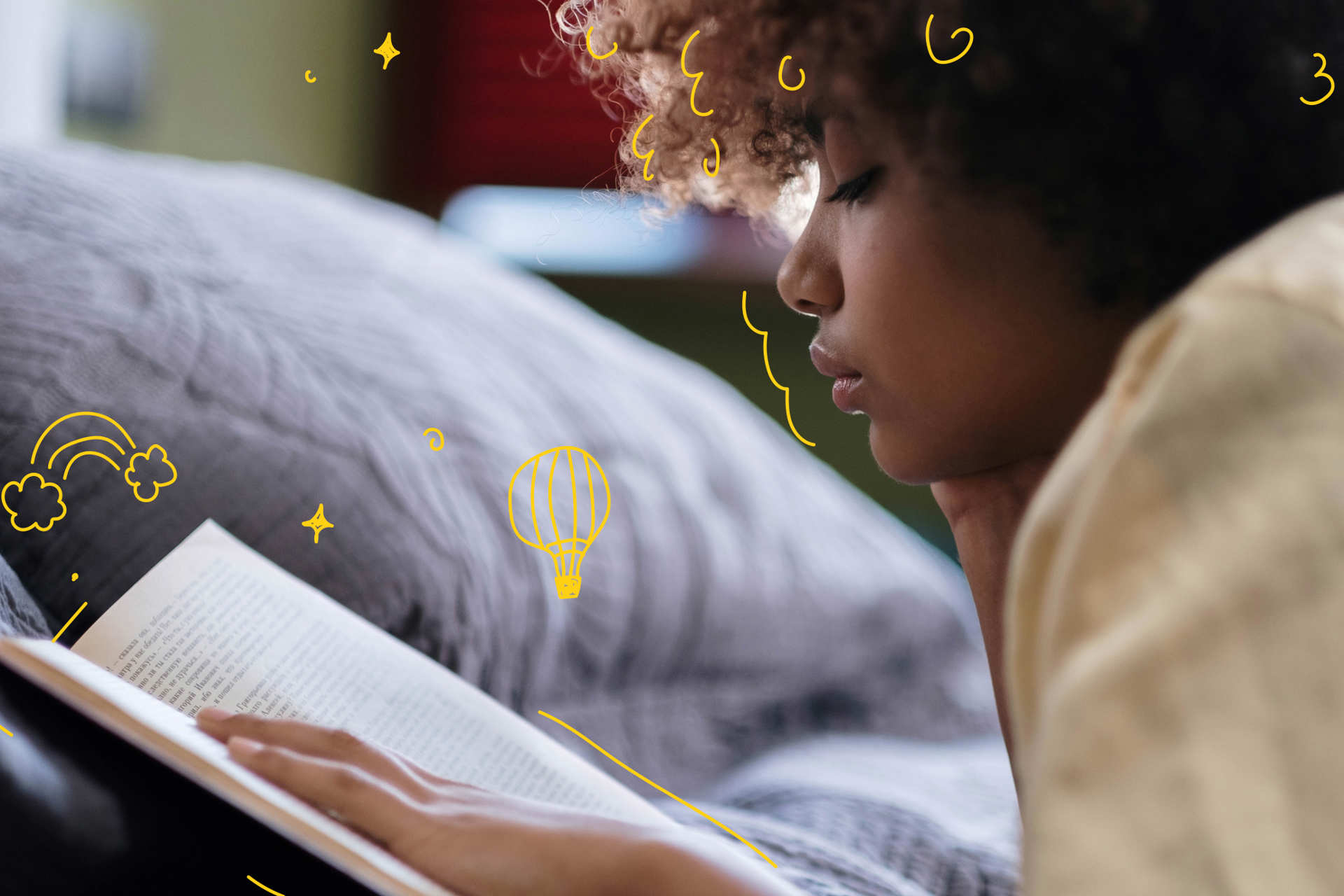 A young person reading a book lying on their front in bed.