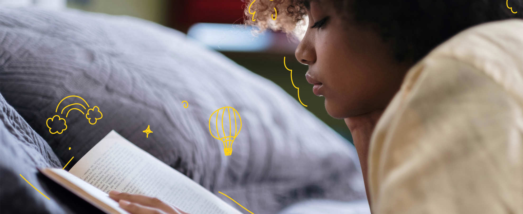 A young person reading a book lying on their front in bed.