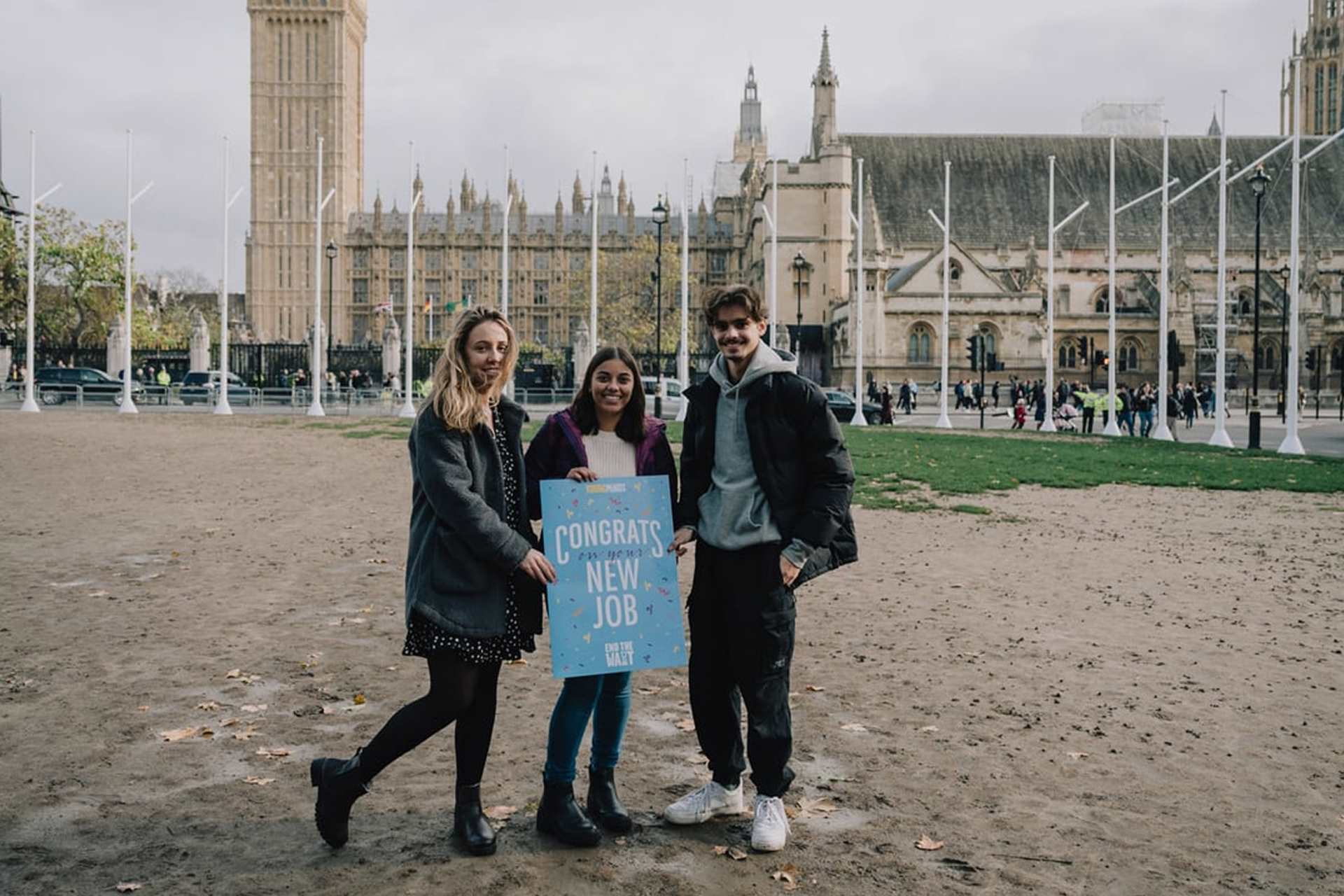 Three YoungMinds Activists standing in front of parliament holding a welcome card saying: 'Congrats on the new job'.