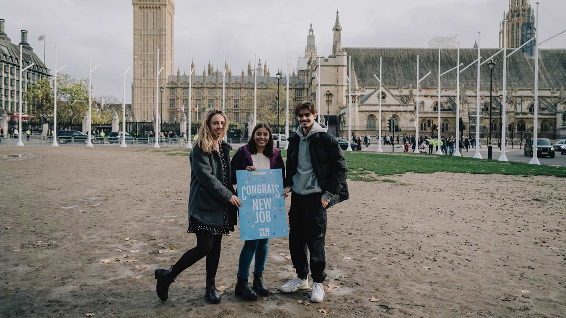 Three YoungMinds Activists standing in front of parliament holding a welcome card saying: 'Congrats on the new job'.