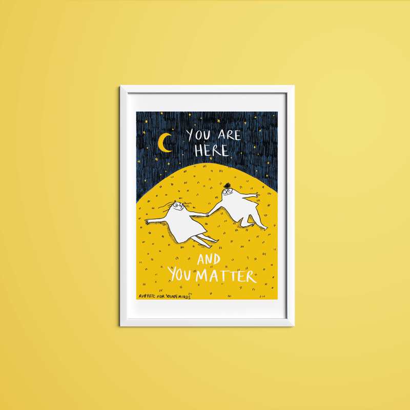 A print by Rubyetc in a white frame with a yellow wall. The print has a night sky at the top with a crescent moon and stars. In the night sky the text reads: you are here. Underneath is a big yellow hill with two people lying on top of the grass. The people are looking at each other and smiling. Underneath the people the text reads: and you matter. In the bottom right hand corner it reads: Rubyetc for YoungMinds.