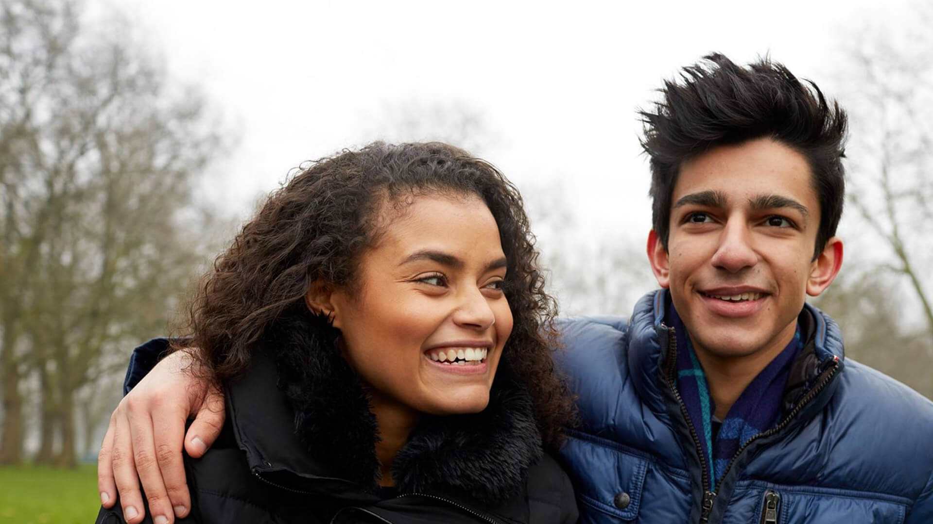 close-up-of-a-young-boy-in-blue-jacket-smiling-while-his-hands-wrap-around-the-shoulder-of-a-girl-with-curly-hair-smiling-while-looking-away