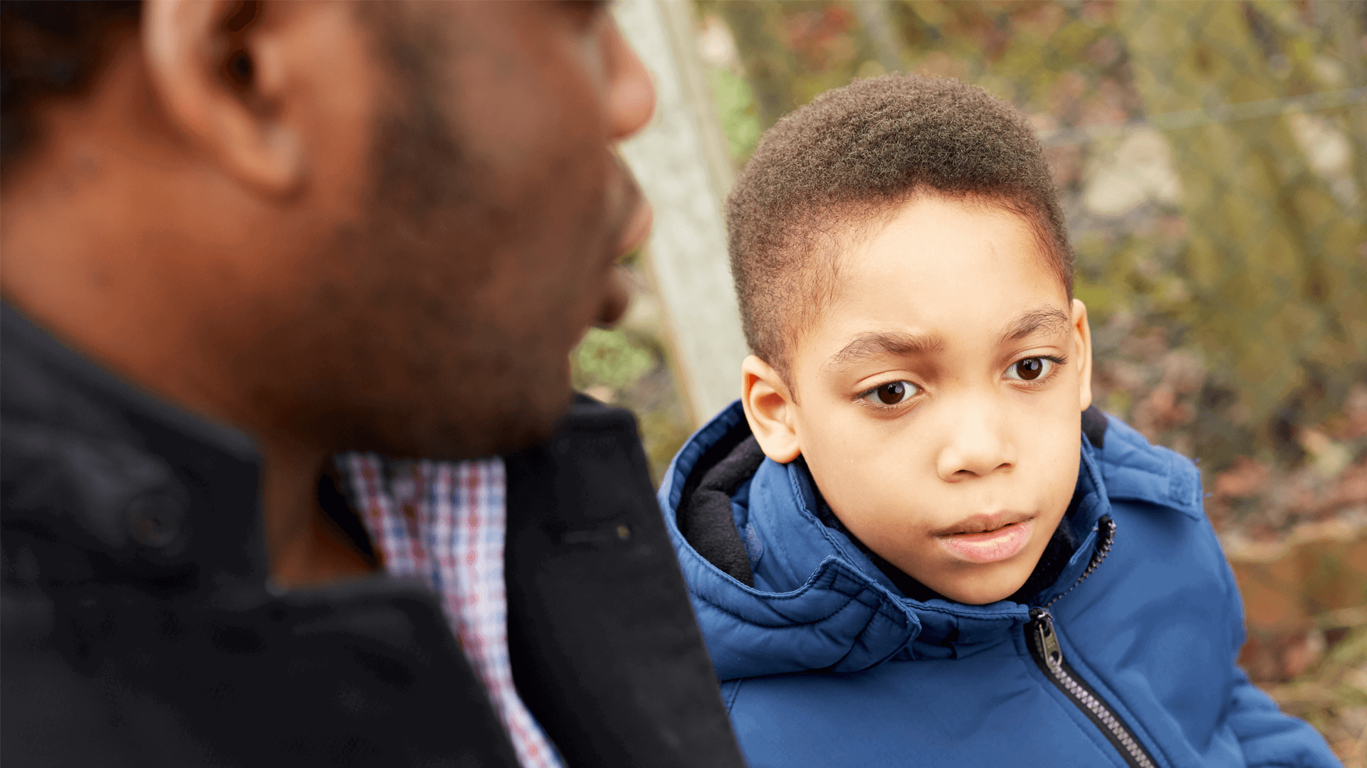 A young boy with his dad outside wearing a blue jacket