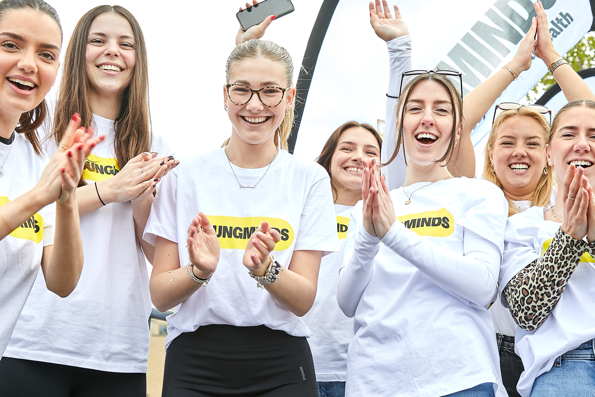 YoungMinds staff cheering marathon runners on from the side line in YoungMinds t-shirts and with YoungMinds banners.