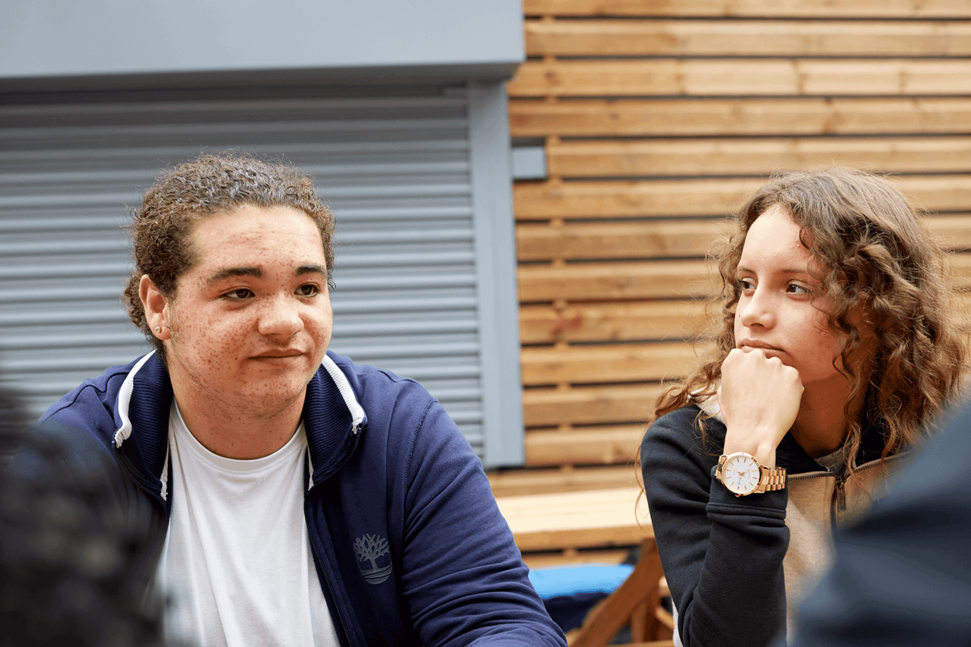 a girl with curly hair and a hand on her chin looking at a boy wearing blue jacket and a white shirt and  looks worried