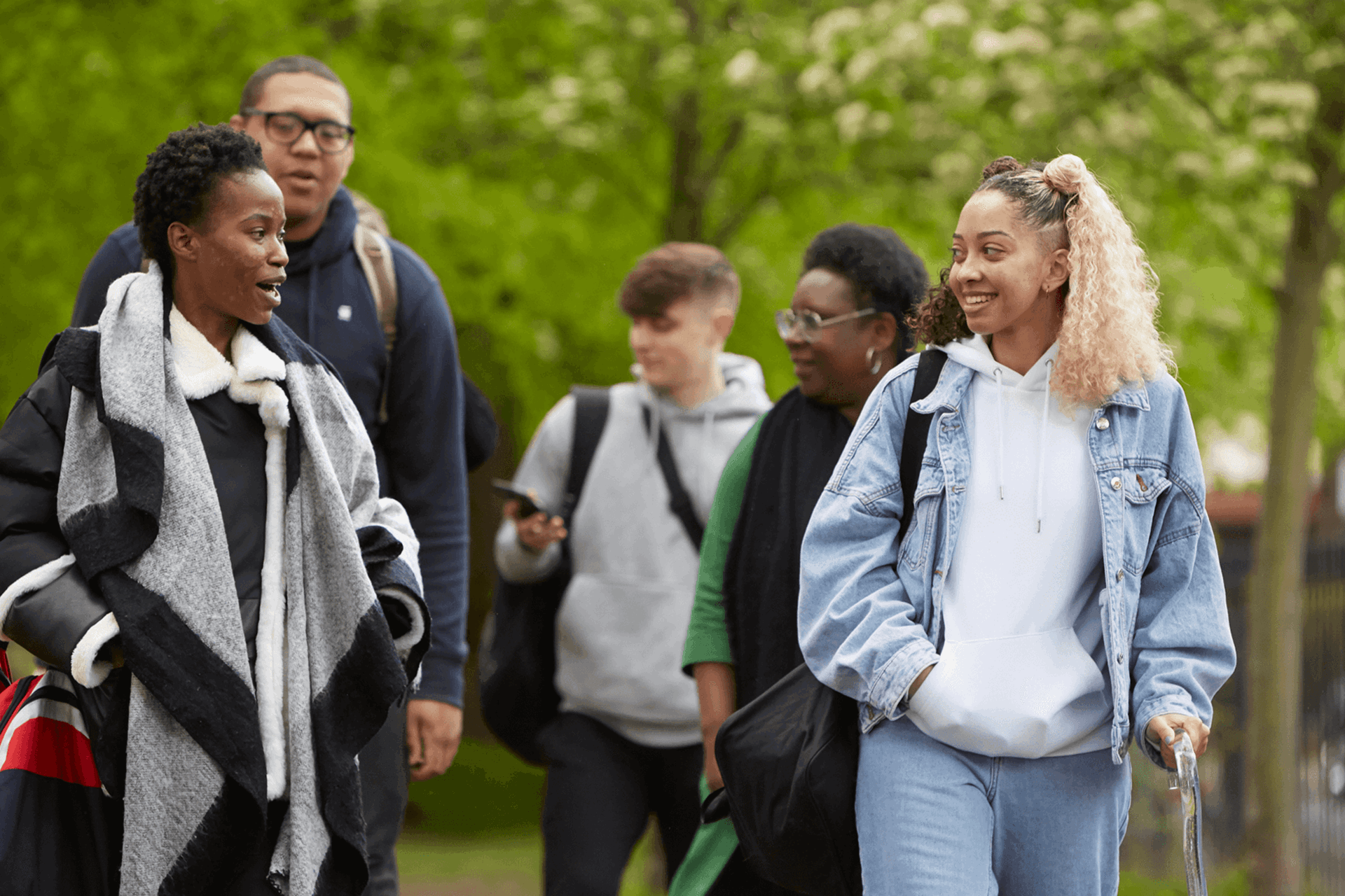 wide-shot-of-five-young-people-talking-and-smiling-while-walking-in-a-park-with-trees