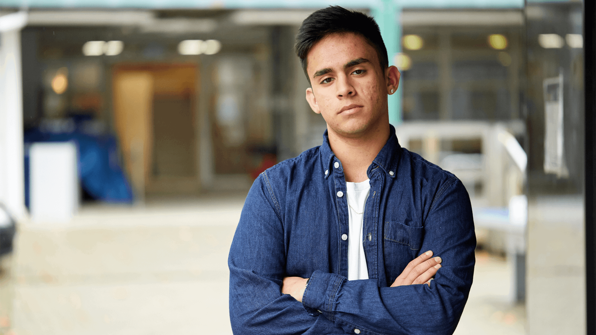 medium-shot-of-a-young-man-looking-in-front-of-the-camera-with-arms-crossed-and-school-campus-on-the-background