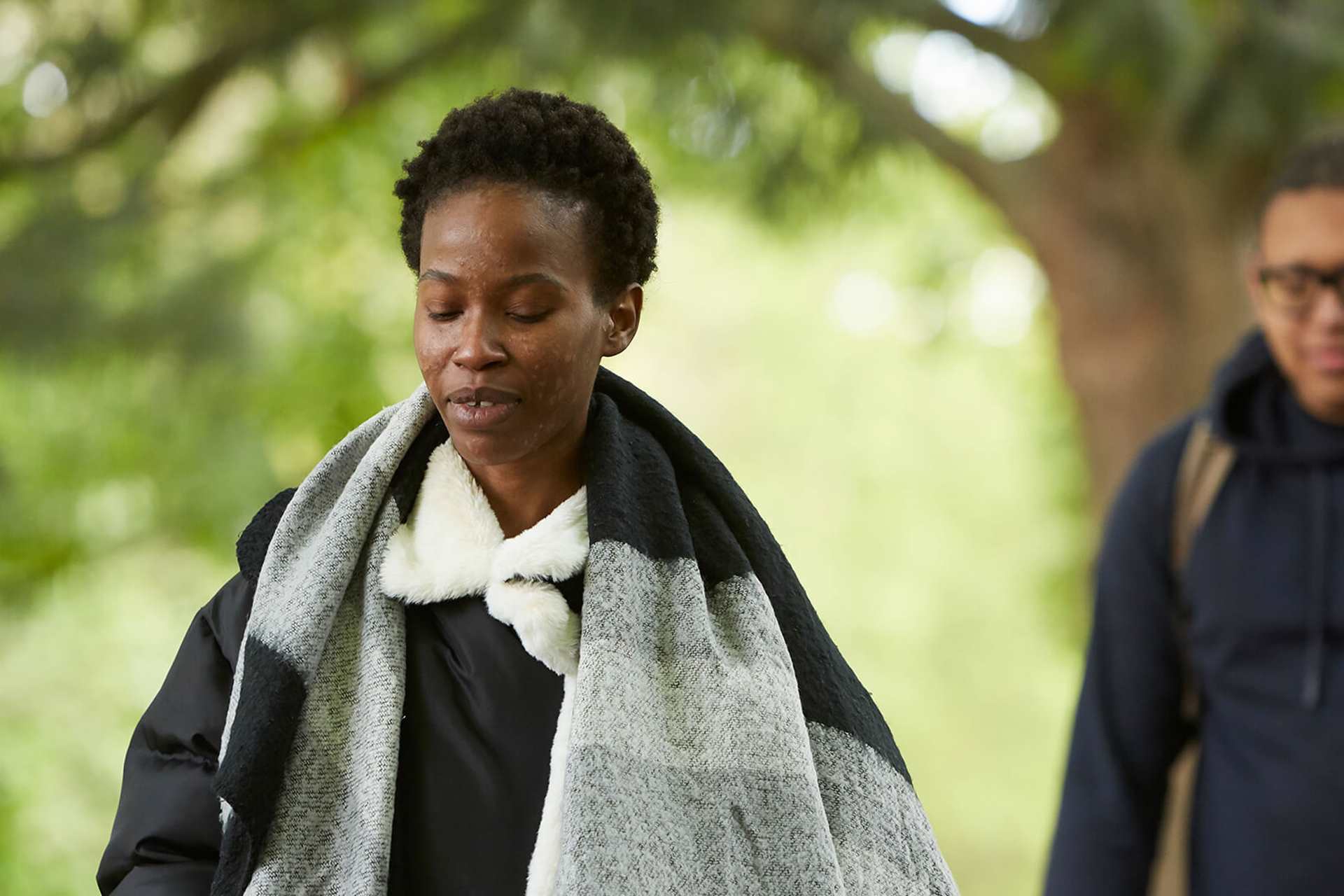 A young woman walking in a park with a friend behind her.