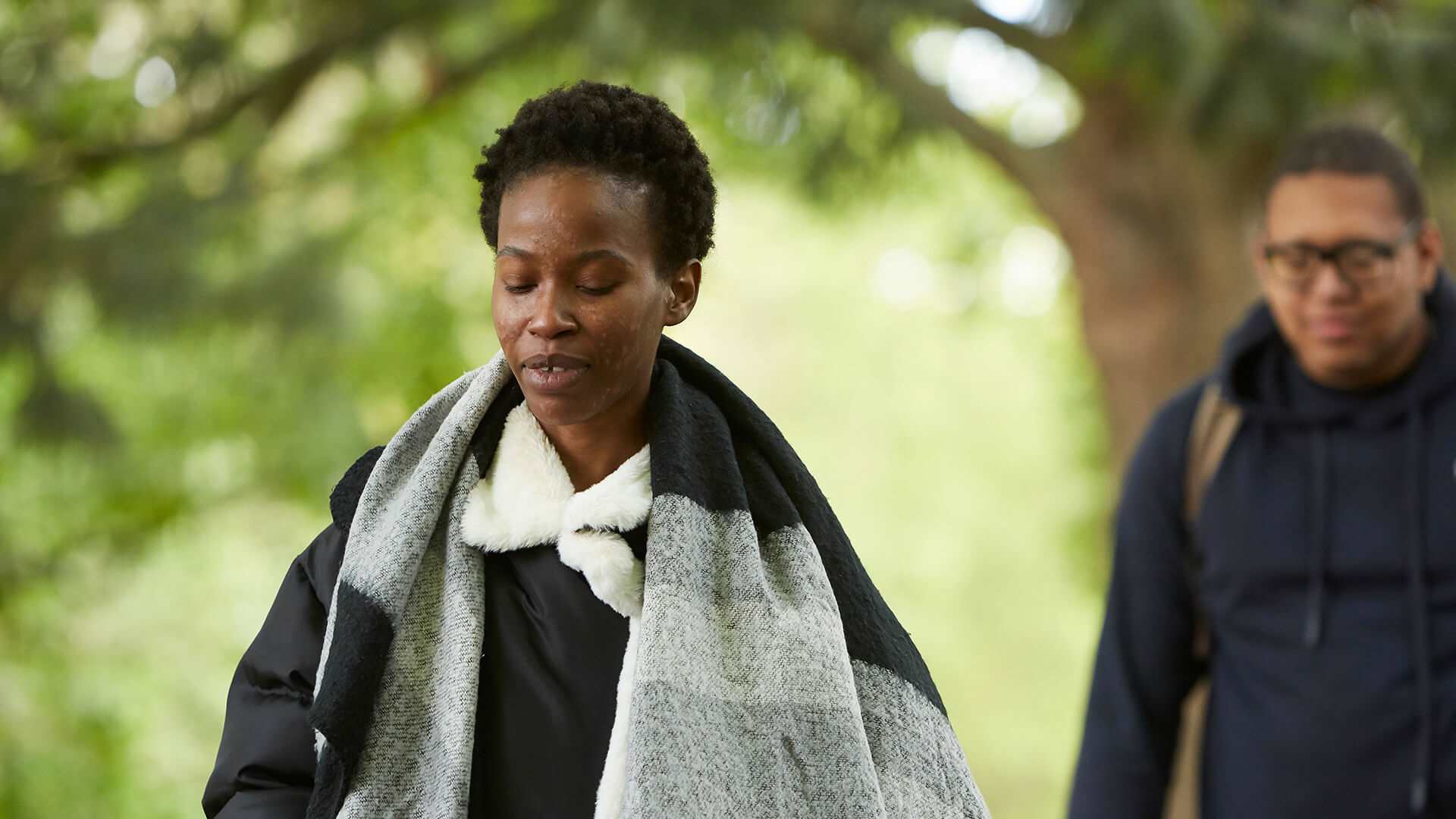 A young woman walking in a park with a friend behind her.