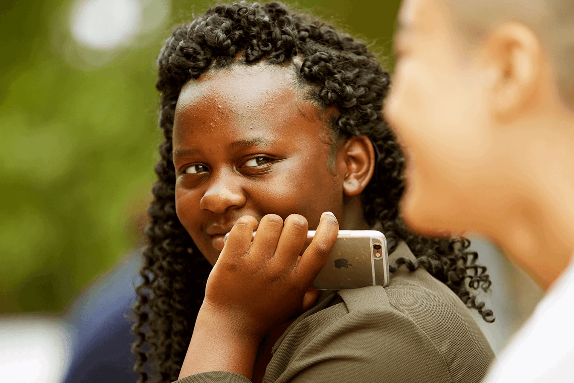 A young person smiling and holding their mobile against their cheek.