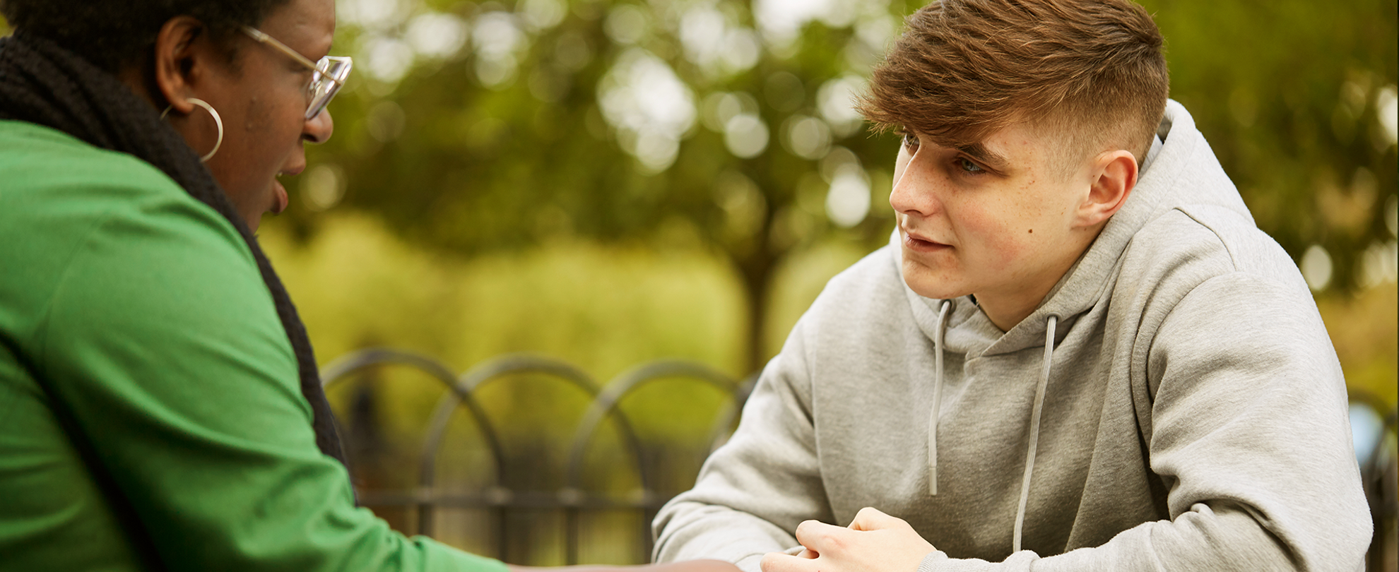 A young person talking to a trusted adult outside on a bench.