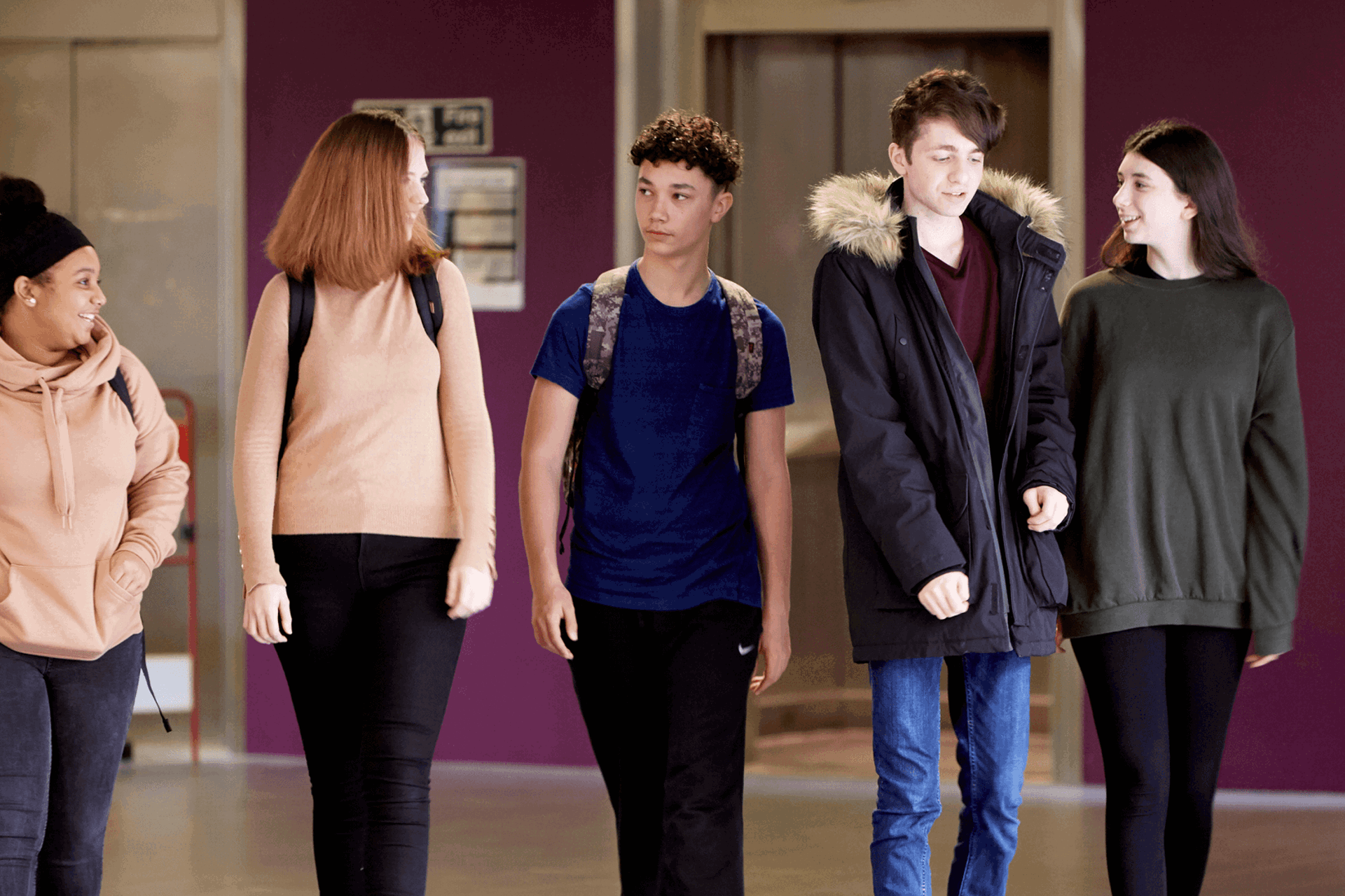 wide shot of five students wearing backpacks walking and talking inside the campus
