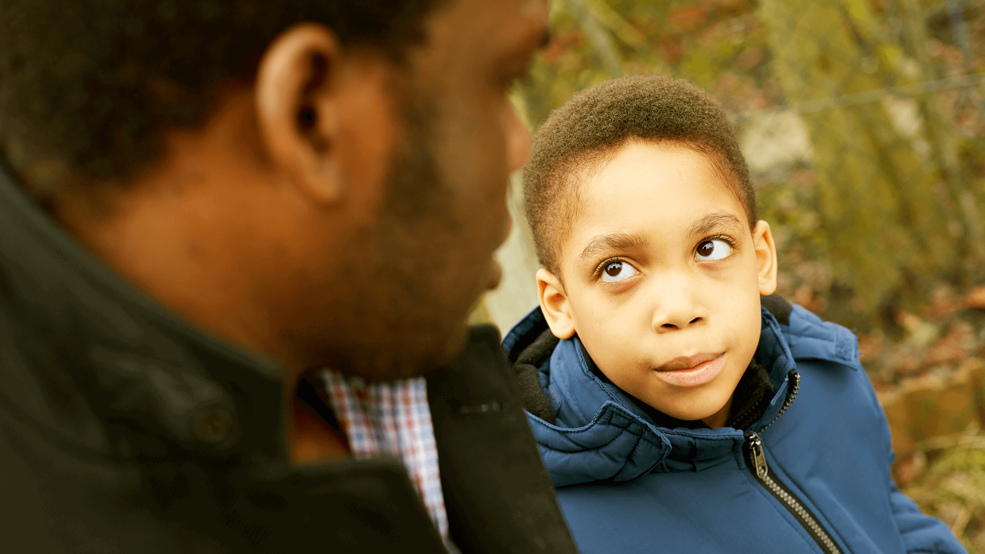 A child sat next to his father and looking up to him.