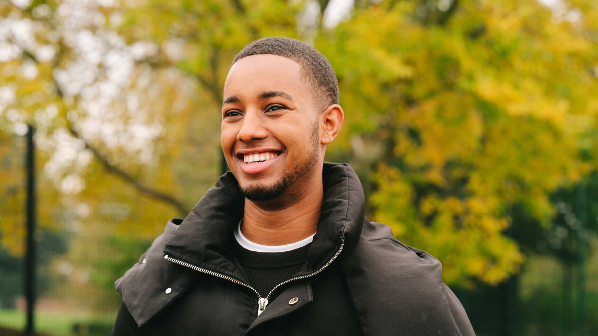 A young Black man smiling in the park.