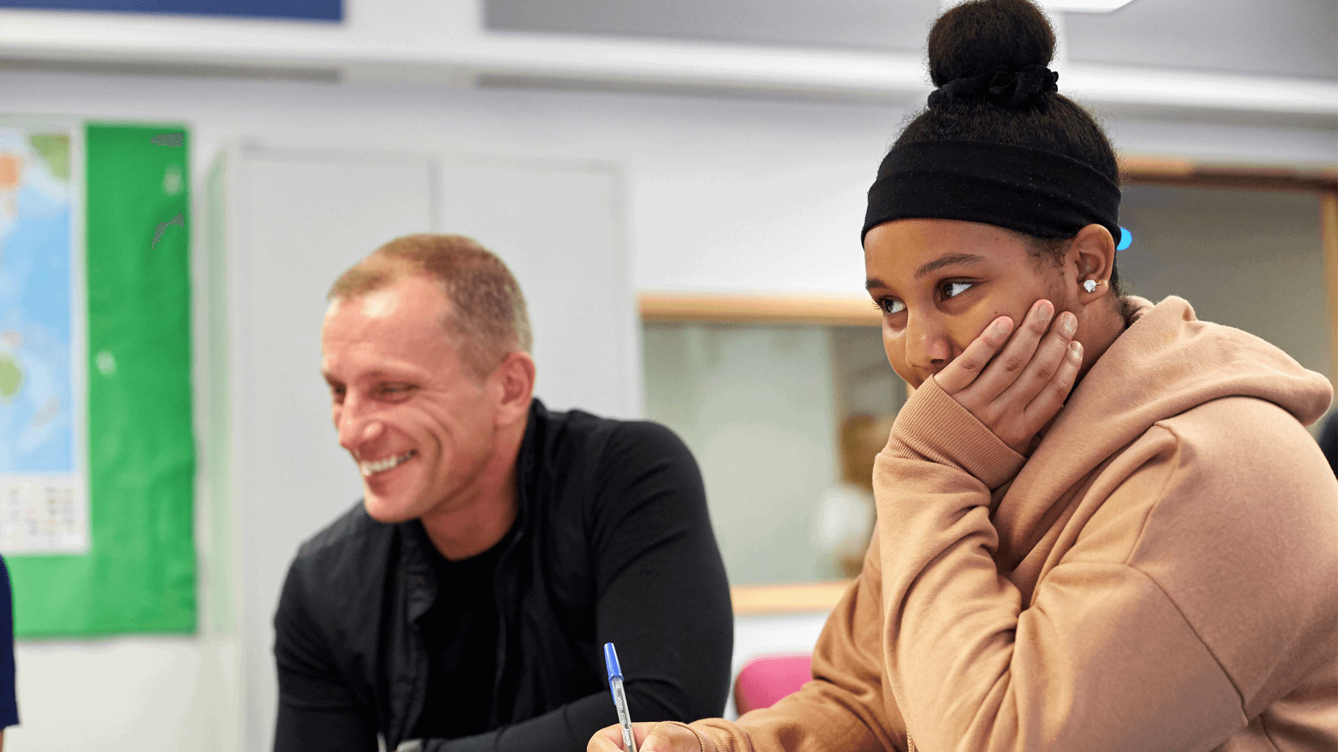 A student sitting at a desk looking amused while taking notes