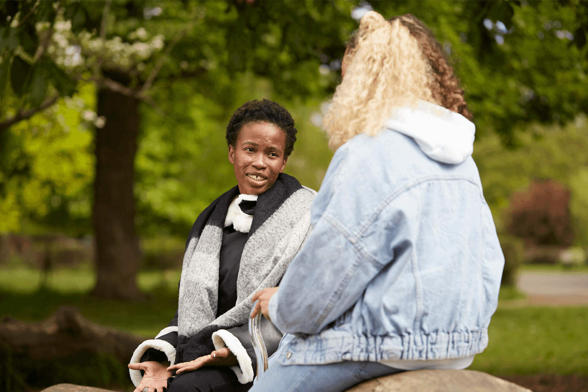 Two young people sitting together in a park and talking to each other.