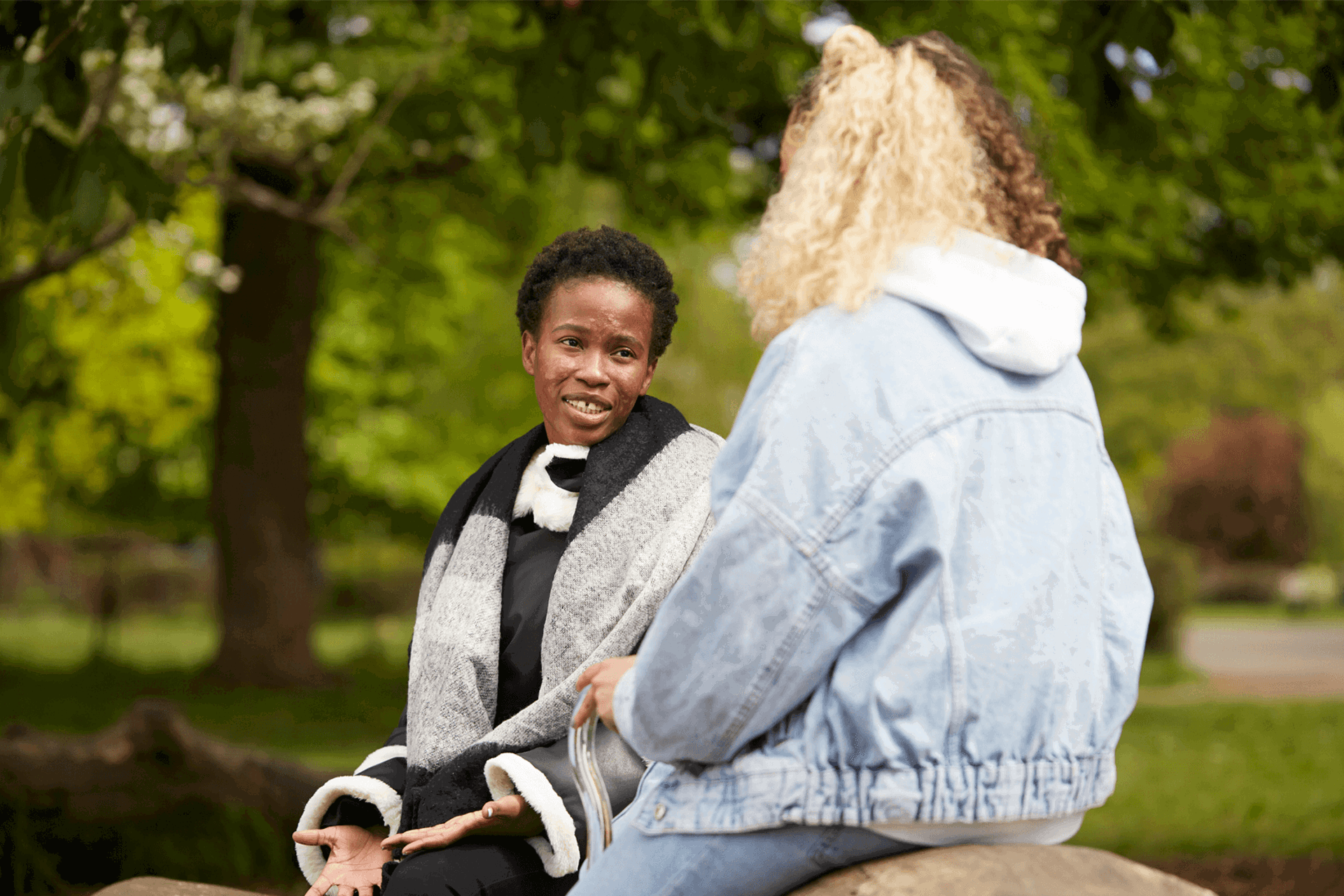 Two young people sitting together in a park and talking to each other.