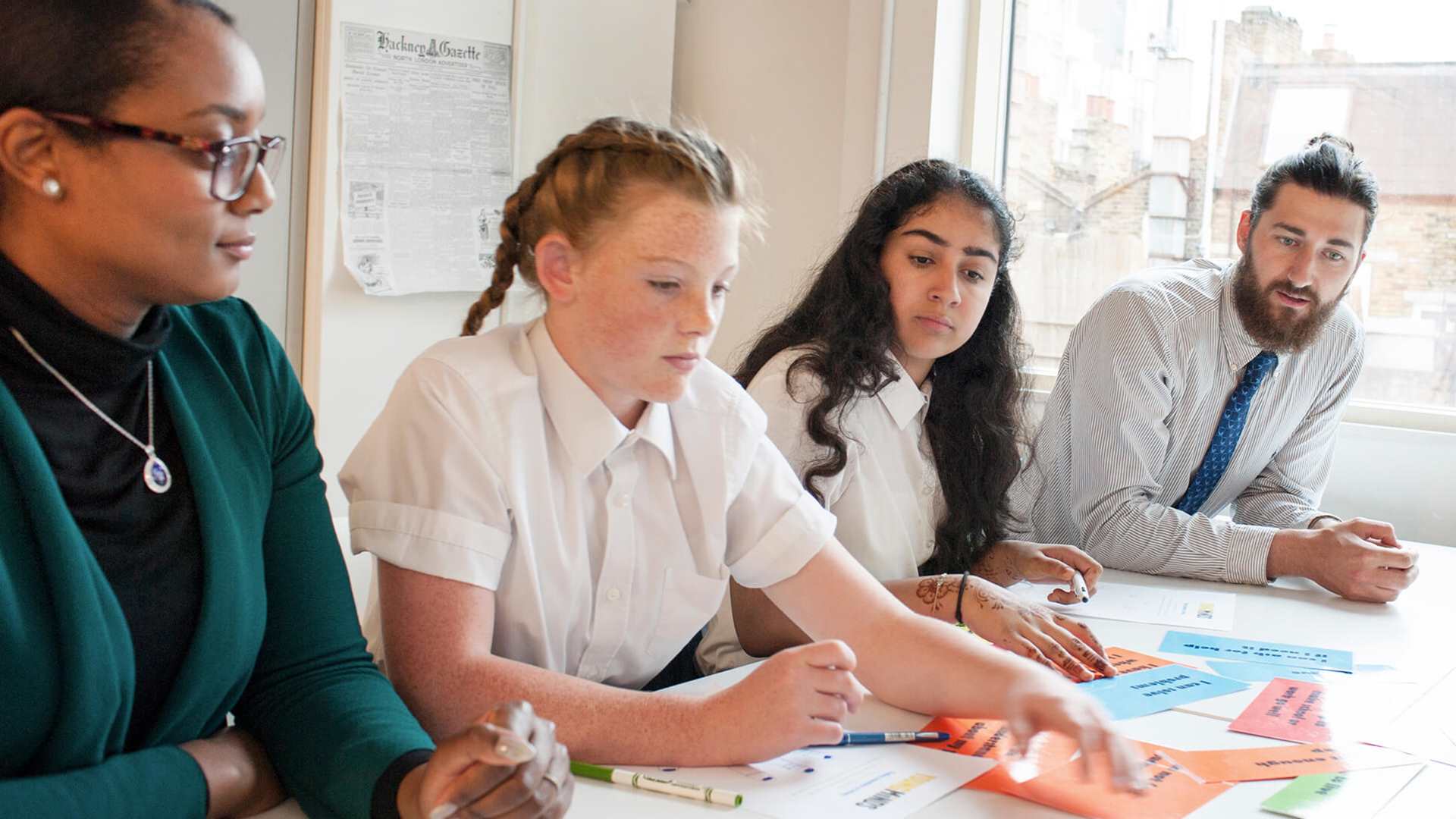 two teachers sits beside two students to guide them while working on an activity with written cards on the table 