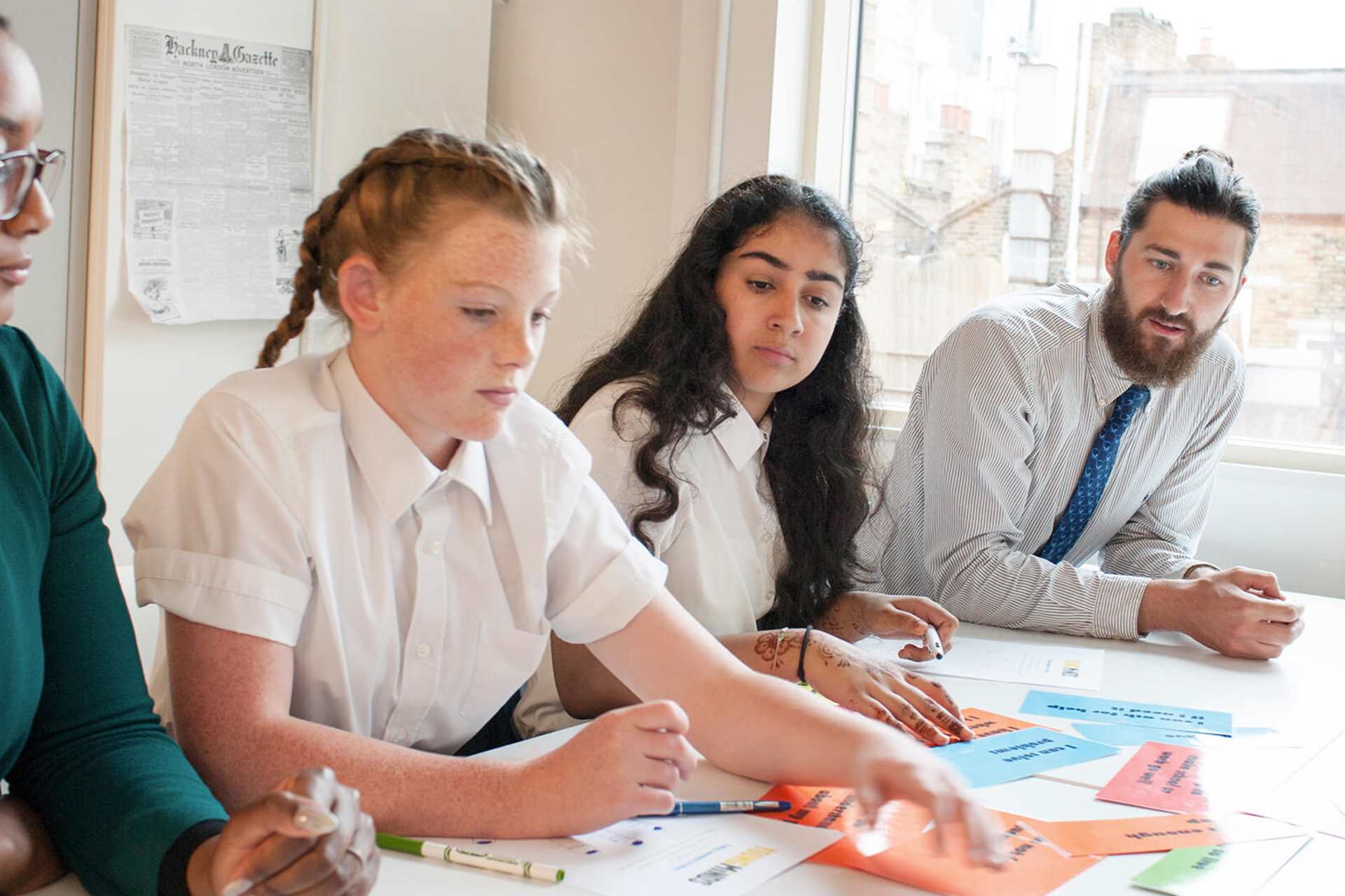 two teachers sits beside two students to guide them while working on an activity with written cards on the table
