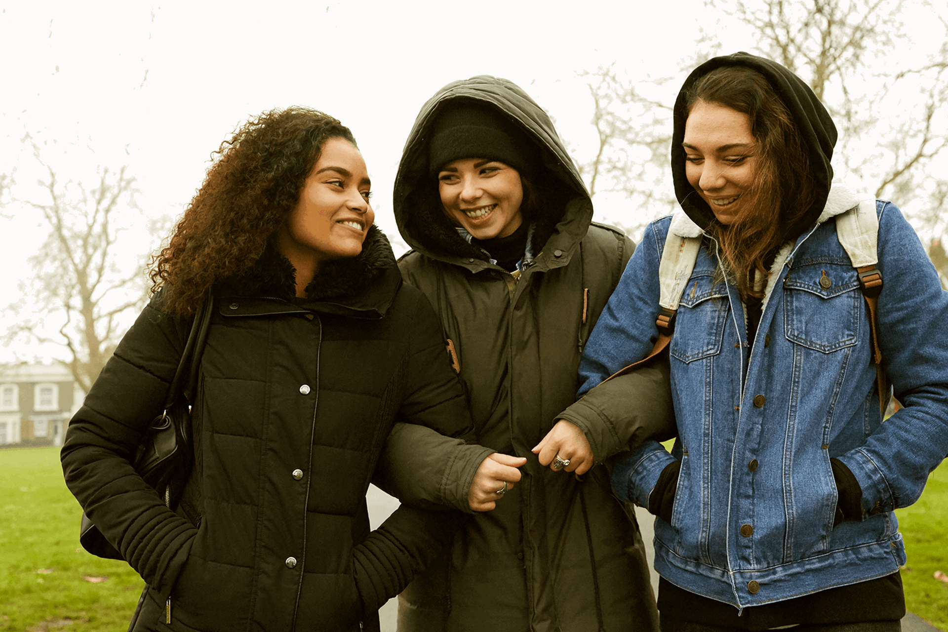 Three young people linking arms and walking through a park together.