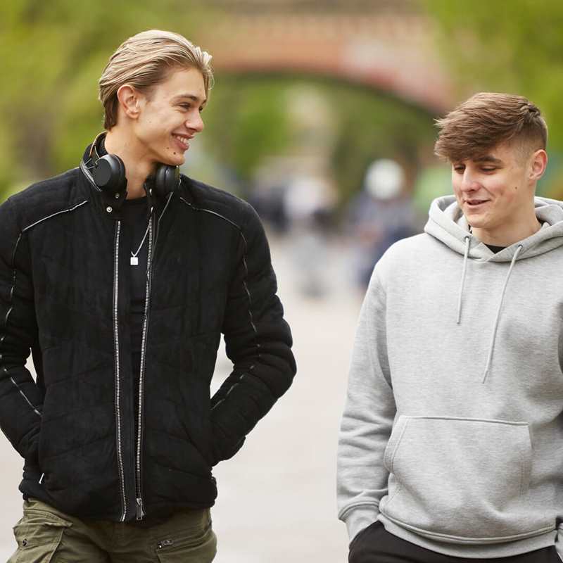 two-young-man-wearing-grey-hoodie-and-black-jacket-walking-and-laughing-on-a-street