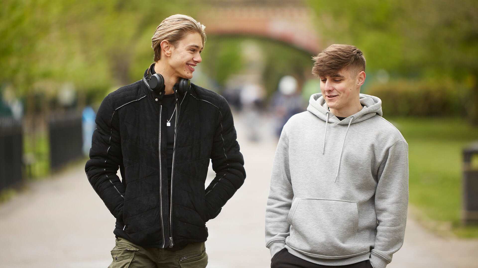 two-young-man-wearing-grey-hoodie-and-black-jacket-walking-and-laughing-on-a-street