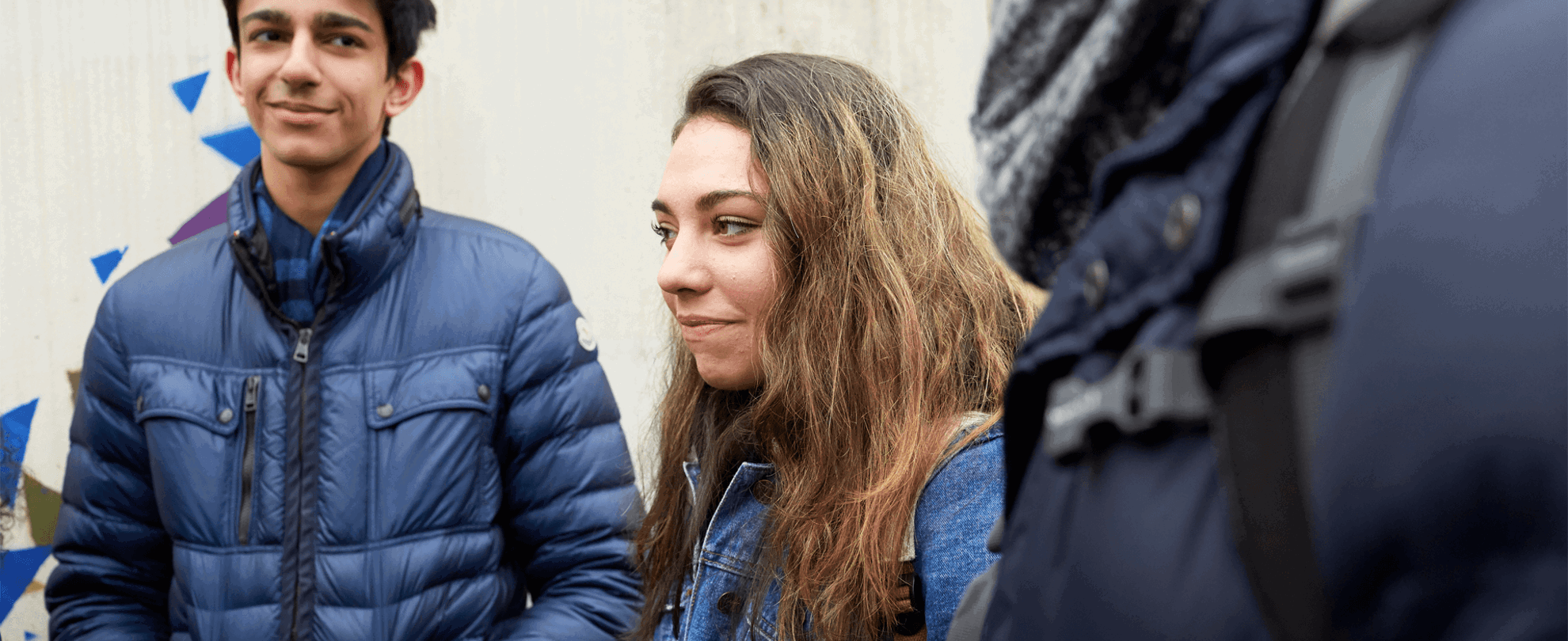 Three young people standing and talking in front of a graffiti wall.