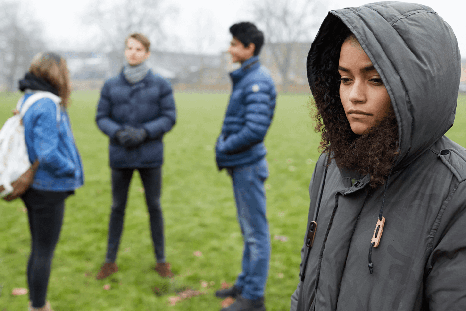 A young person stands alone feeling left out by three friends standing together.