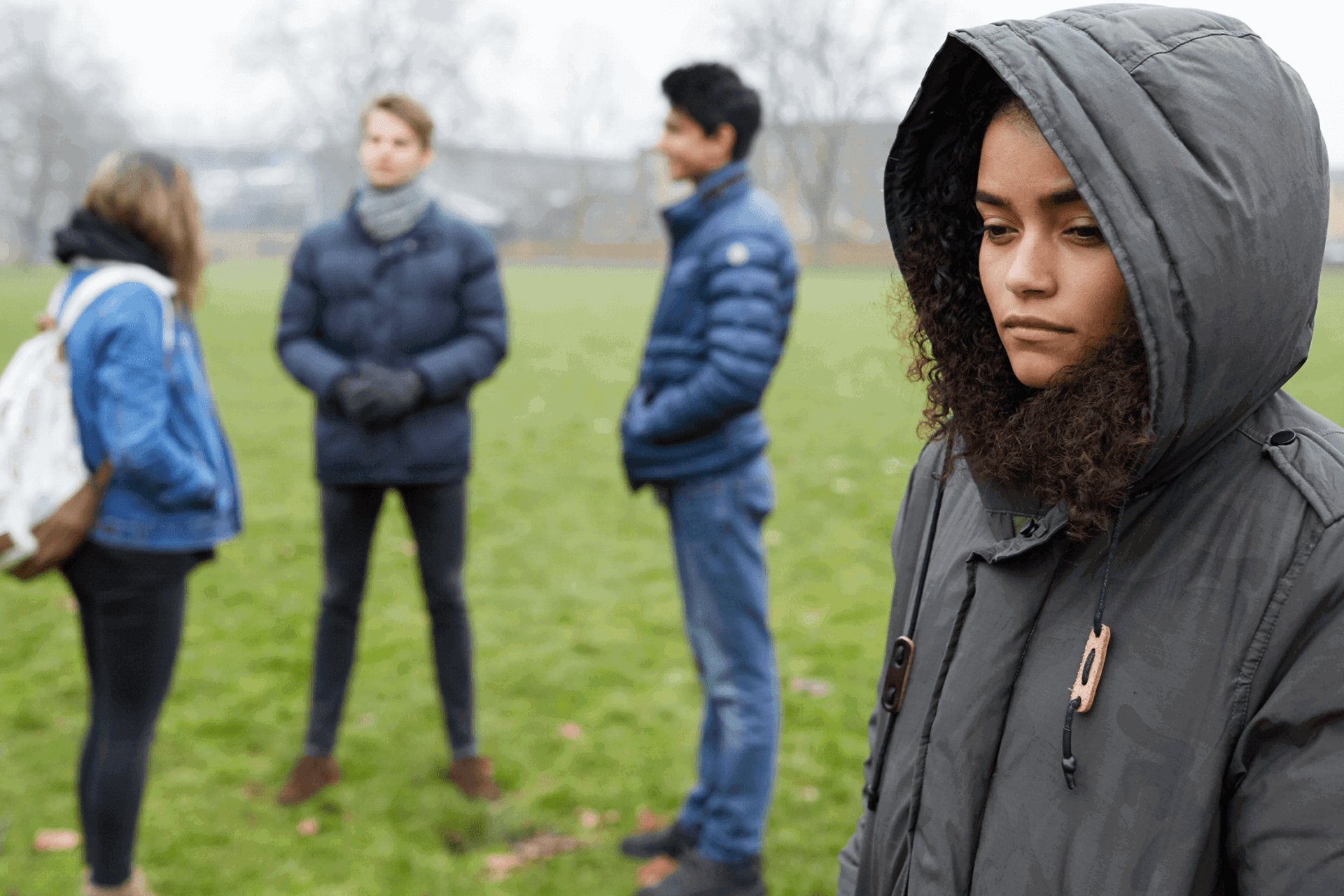 A young person stands alone feeling left out by three friends standing together.