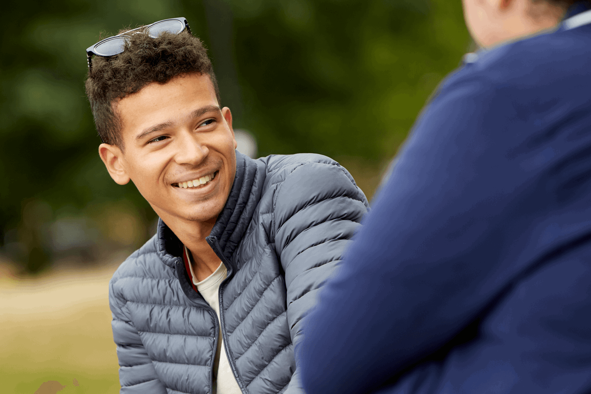 A boy wearing black jacket and smiling as he looks to his friend beside him.