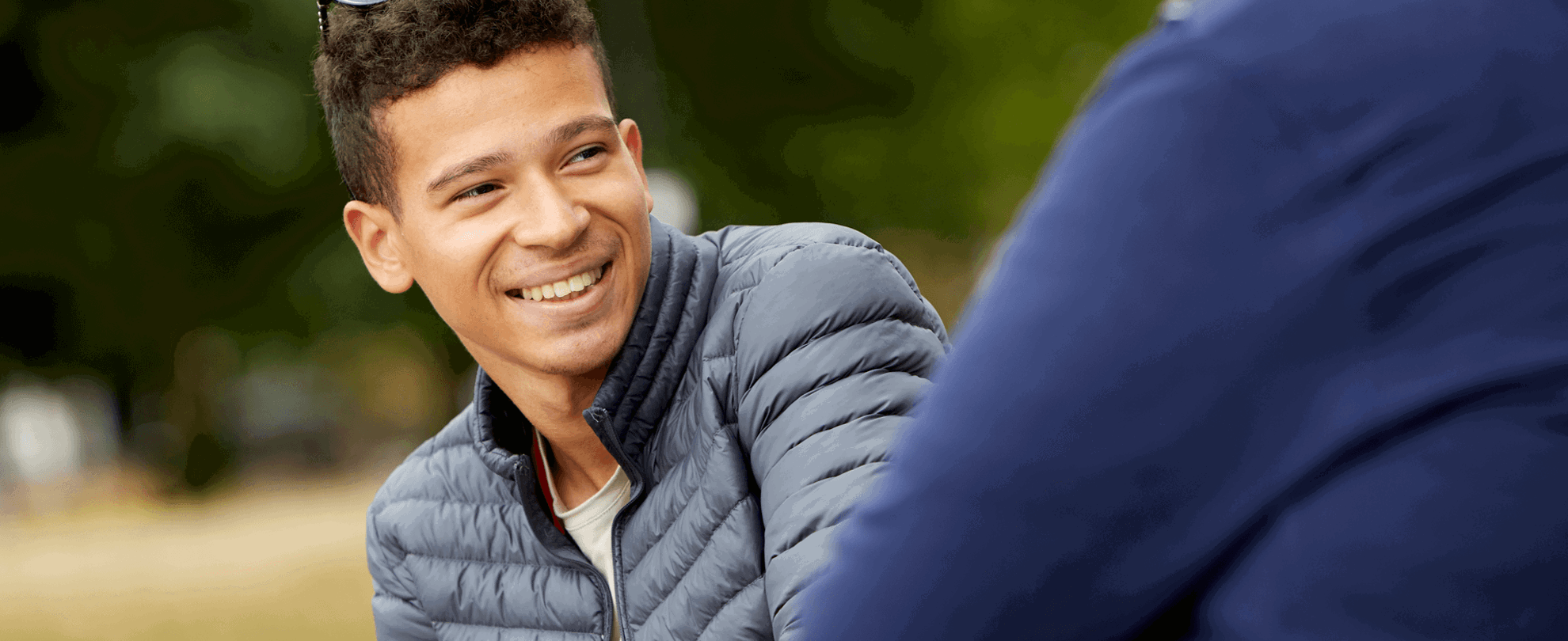 A boy wearing black jacket and smiling as he looks to his friend beside him.