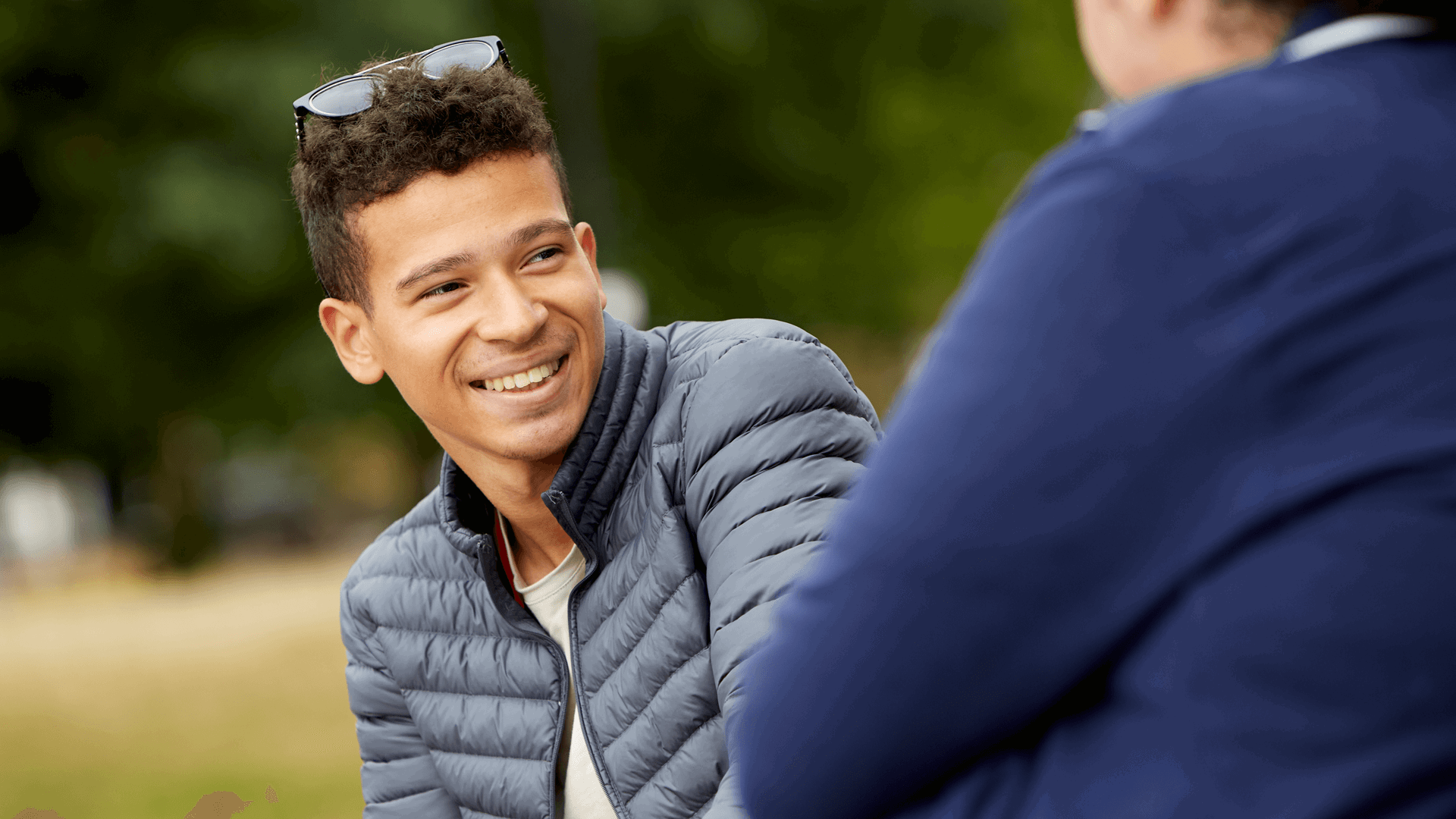 A boy wearing black jacket and smiling as he looks to his friend beside him.