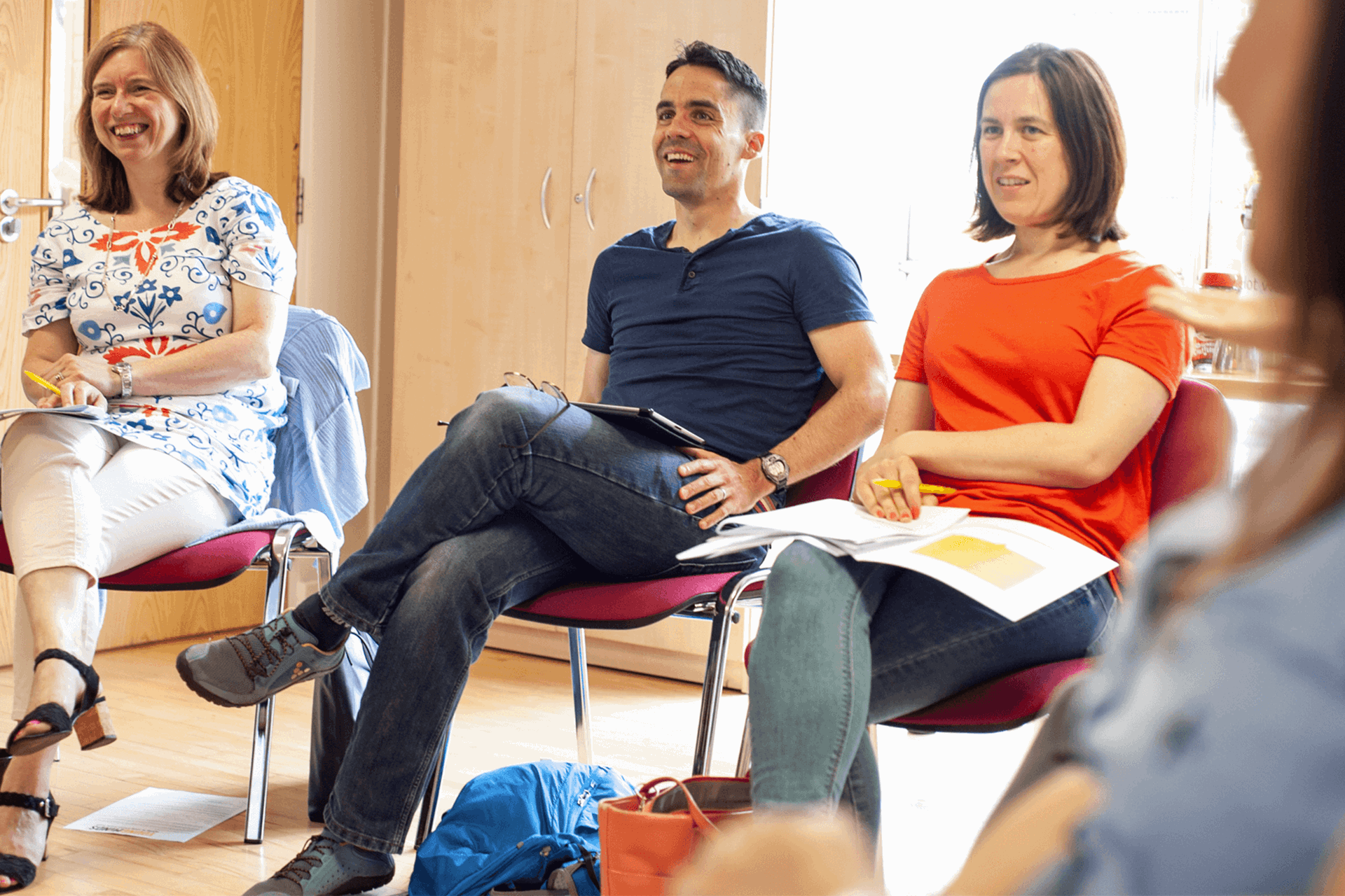 a group of parents sits in circle and laughing during  a workshop inside a classroom