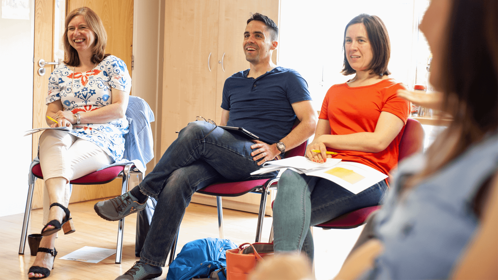 a group of parents sits in circle and laughing during  a workshop inside a classroom