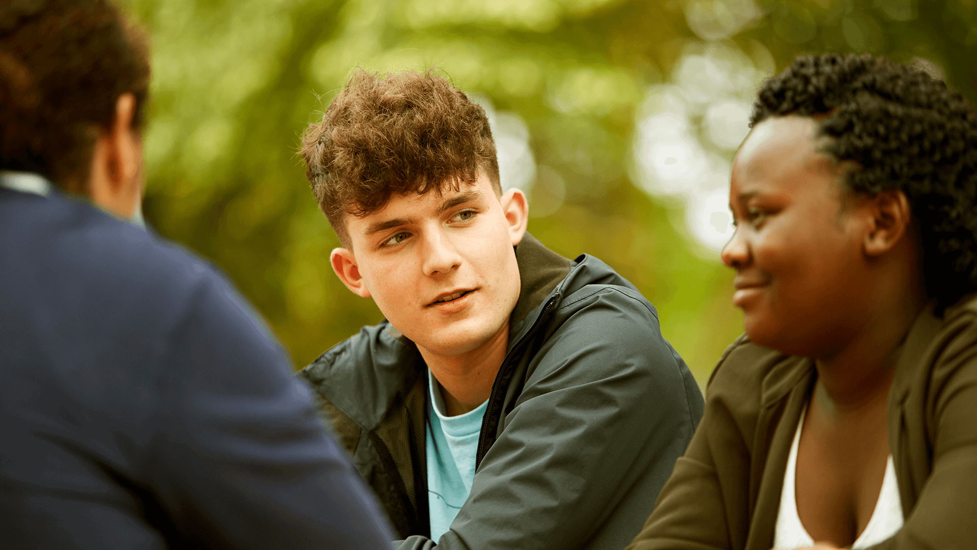 Three young people sitting together in a park.