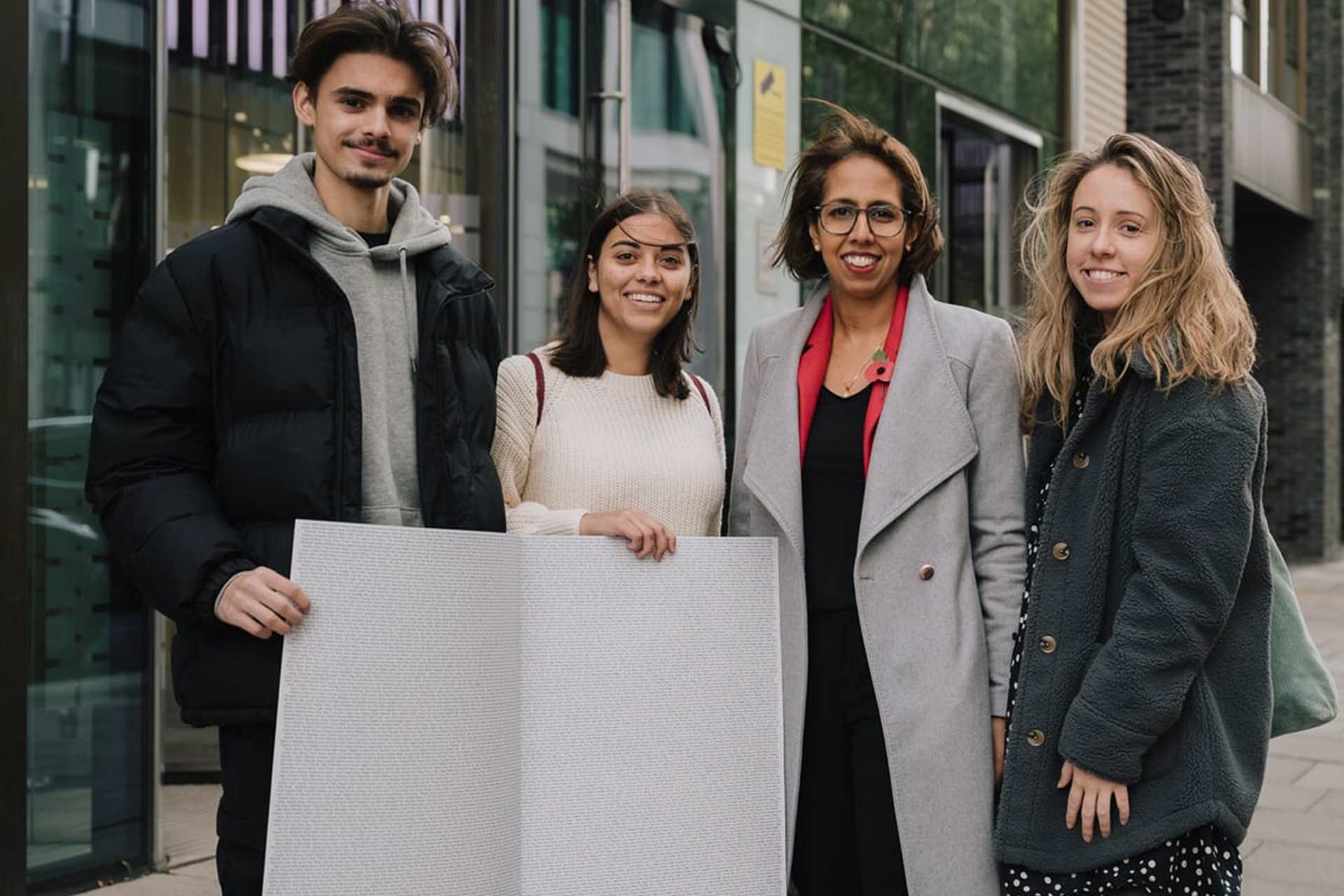Three YoungMinds Activists with MP Munira Wilson holding the End The Wait card open on a page with all the signatures.
