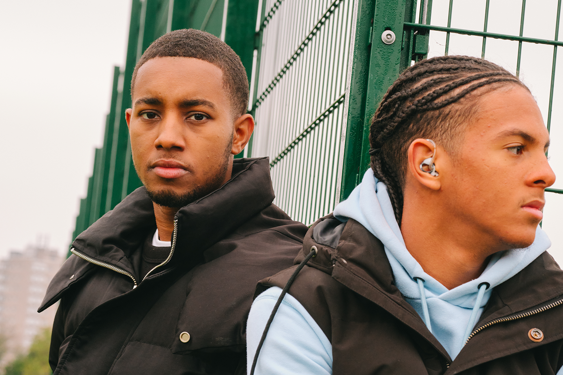 A young Black man sitting in the park with a Black teenage boy wearing a hearing aid. They are both looking very serious.