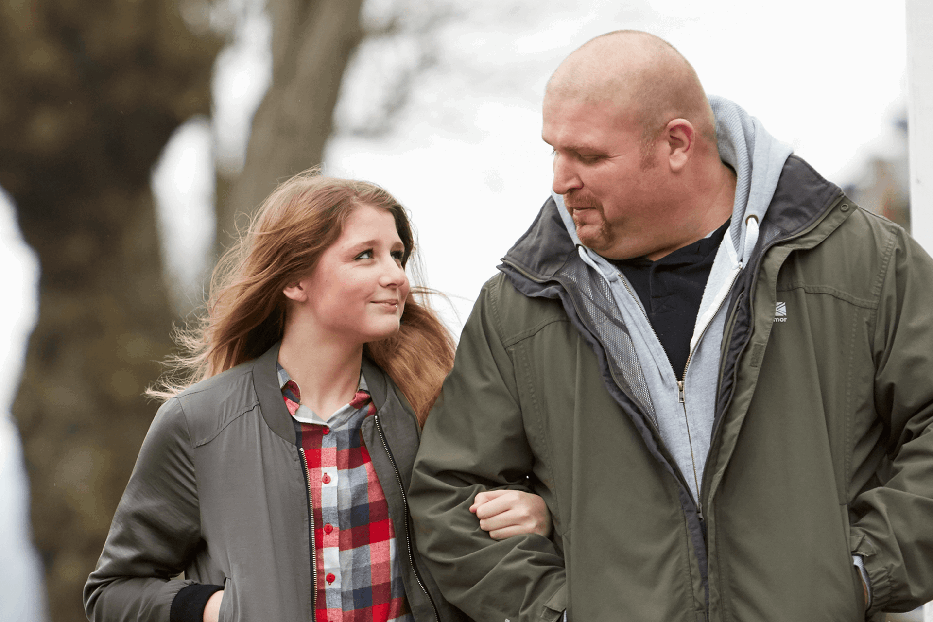 A father and daughter linking arms near a tree