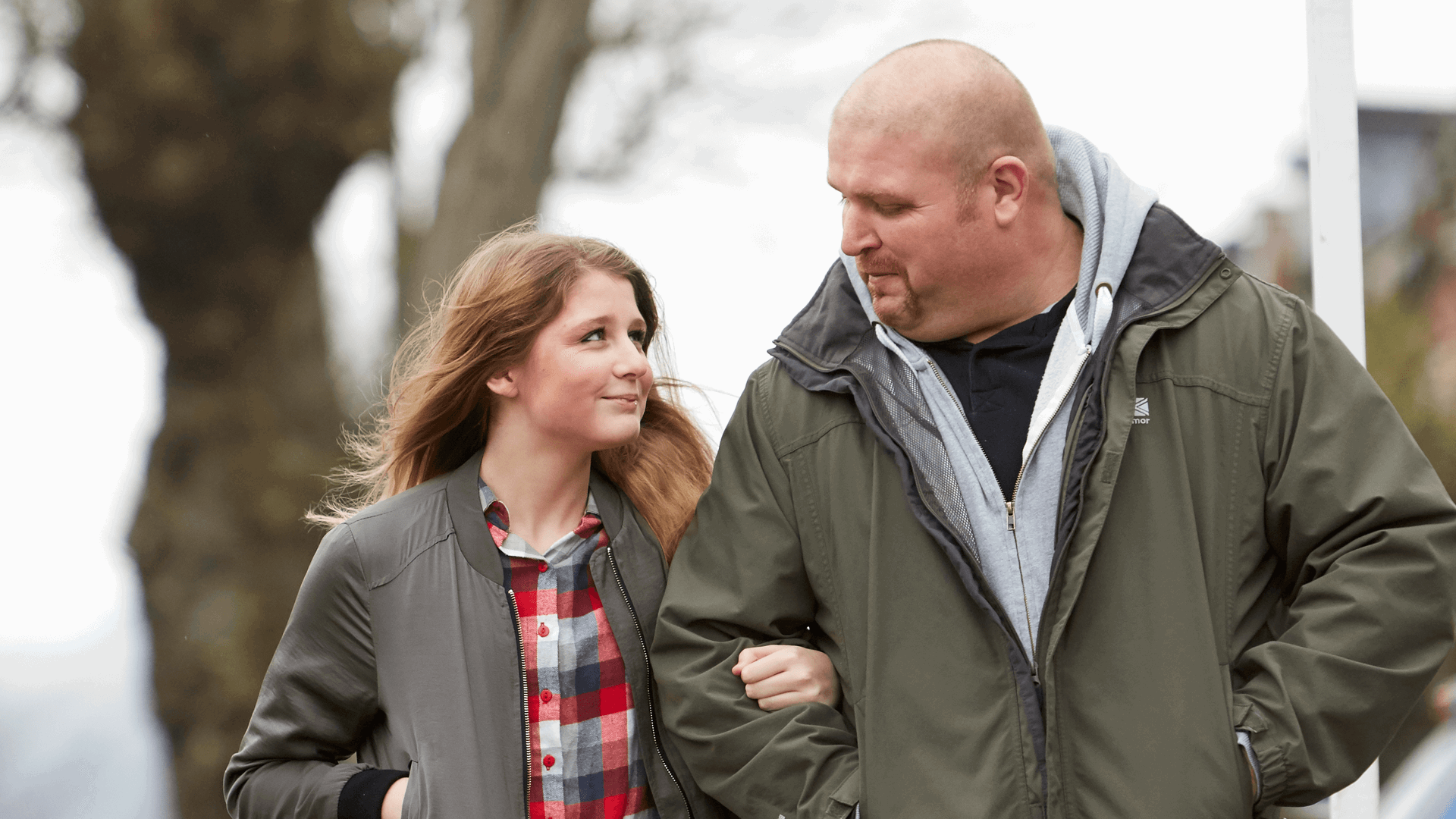 A father and daughter linking arms near a tree