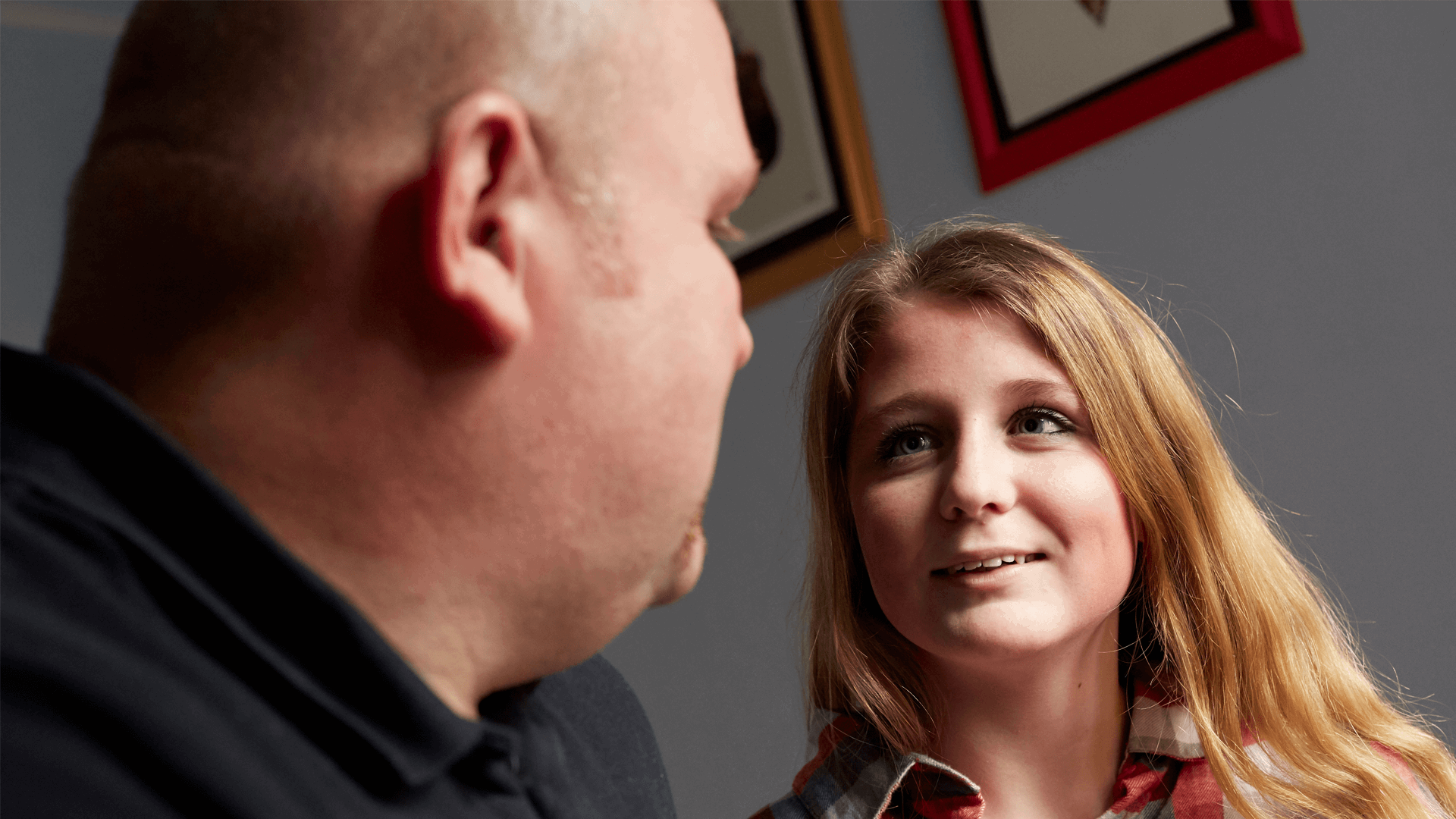 A young girl speaking to her father in front of a wall with pictures hanging behind them