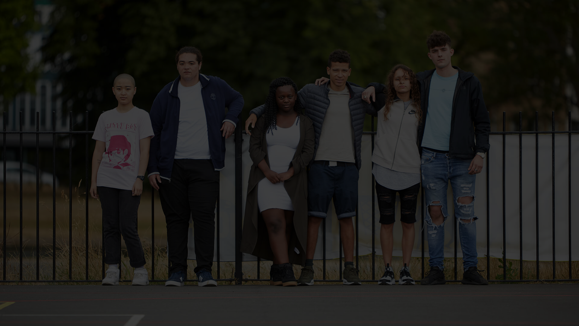 A line of young people standing against a fence outside.